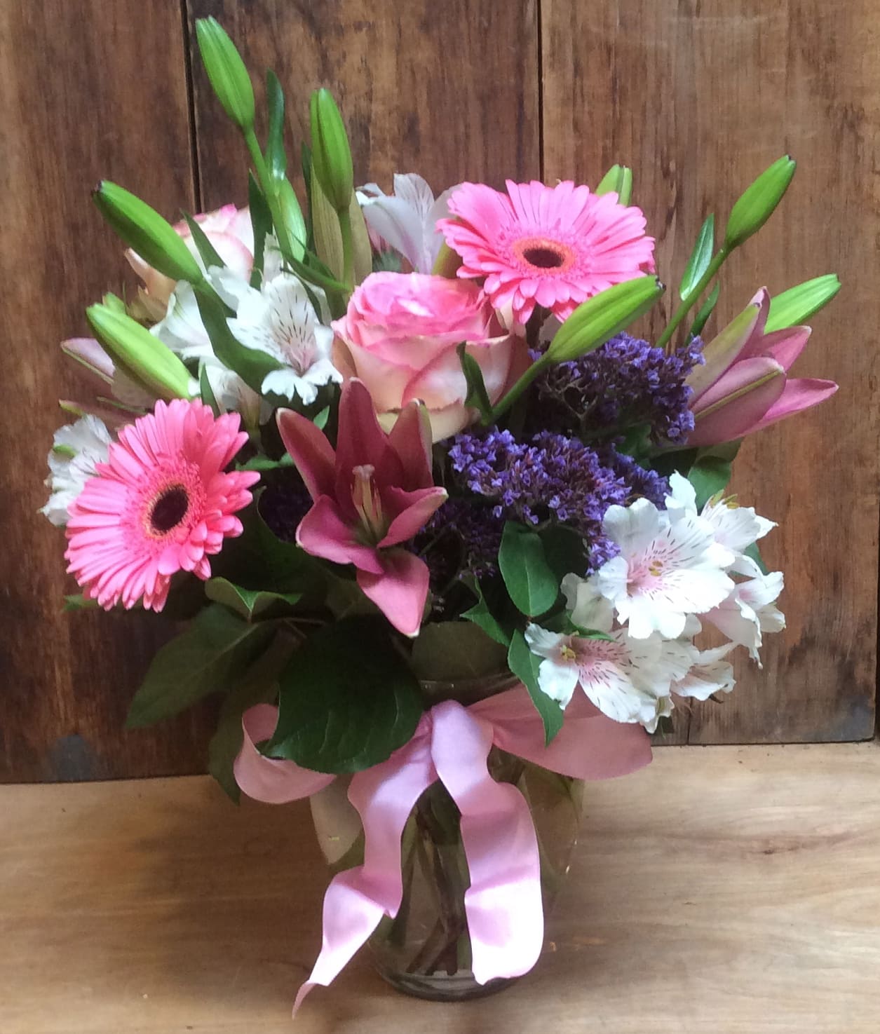 Lovely Lovely - Send someone on a walk through an enchanted English garden with this country style arrangement! Delicate textures, feminine flowers and soft pinks give it a shabby chic look she'll love! A lush variety of flowers - roses, lilies, alstroemeria, gerbera, - are arranged in a more traditional airy style with some height in a clear glass ginger vase and french ribbon bow. approx 15" tall