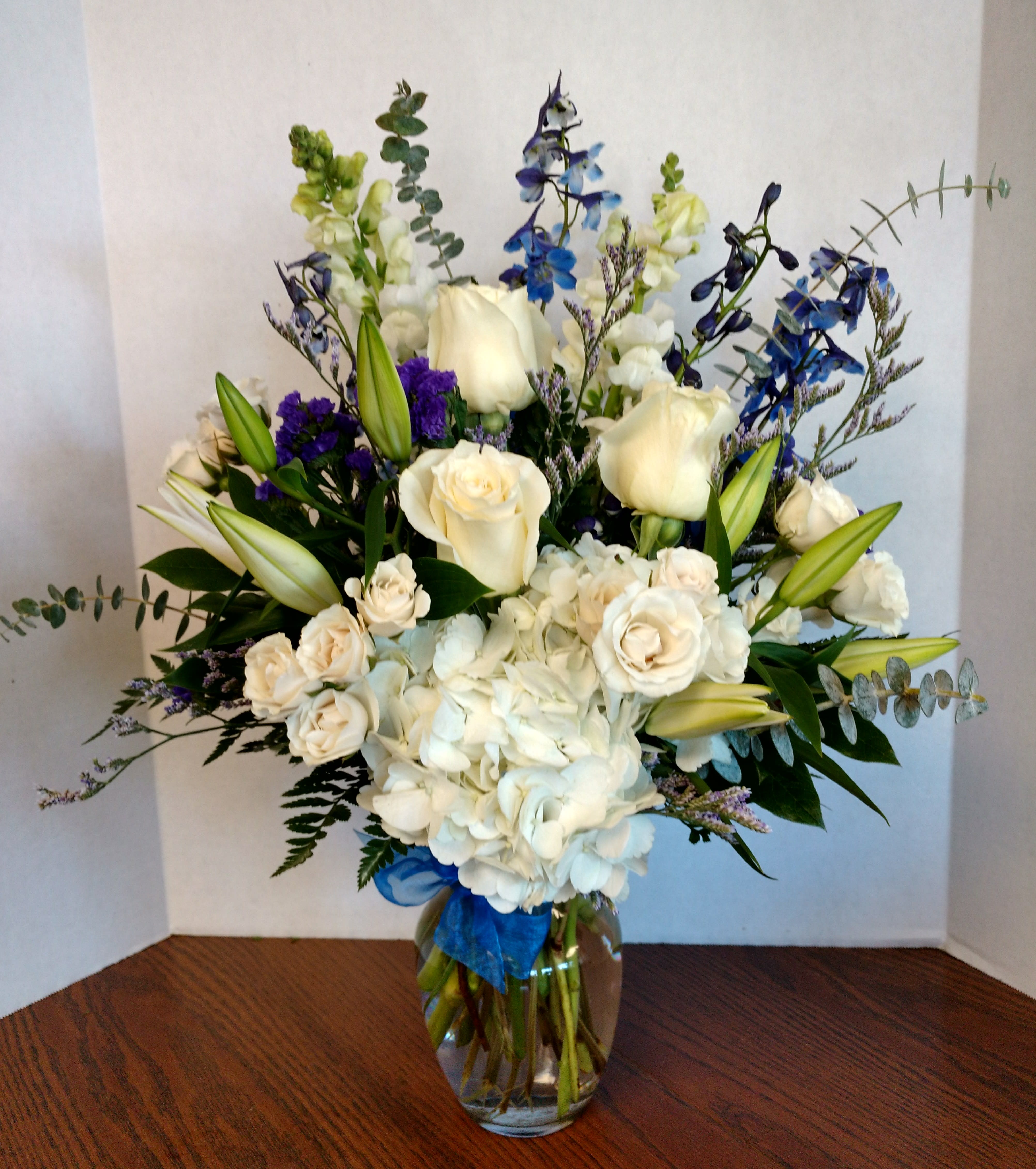 Blue Sky by Candlelight &amp; Roses - Elegant floral vase of white and soft touches of blues.  Featuring hydrangea, roses, delphinium, lily's with lush greens and trim.  Lovely sympathy gift as well as all occasion. Order this flower delivery today