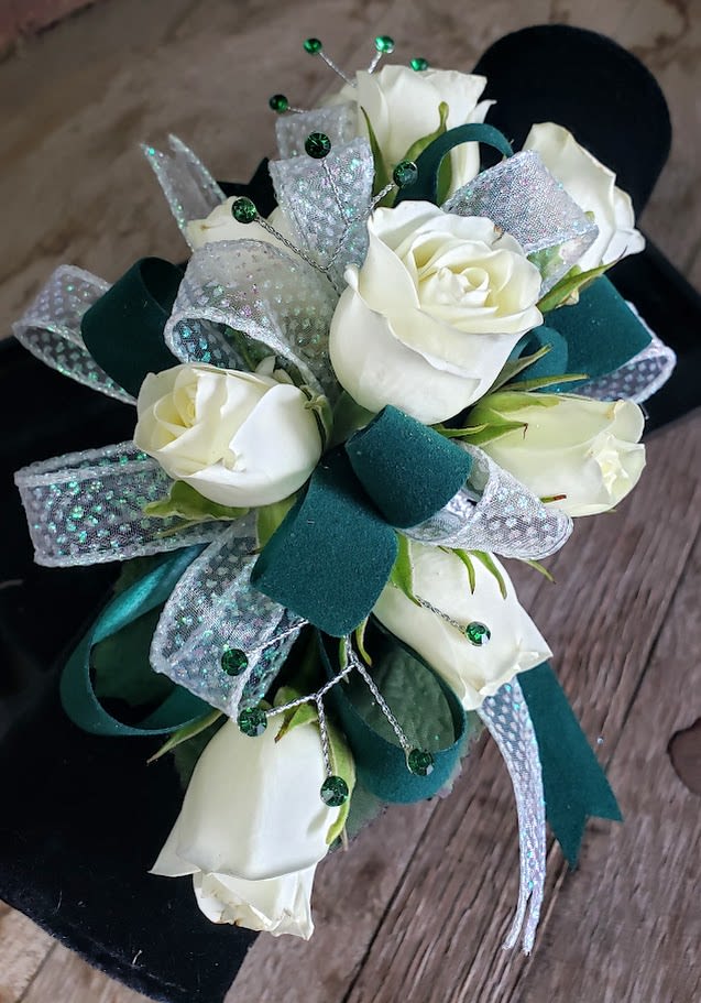 Emerald Elegance wrist Corsage Emerald Elegance wrist Corsage - This corsage is serving timeless sophistication with a touch of sparkle. Featuring crisp white spray roses nestled against deep emerald green ribbon, it’s finished with shimmering accents and scattered rhinestones for that extra flash of luxe. The perfect blend of grace and glamour, it catches the light—and attention—at every turn. Ideal for prom, galas, or any event where you want to look effortlessly regal. Because elegance should always come with a little shine.