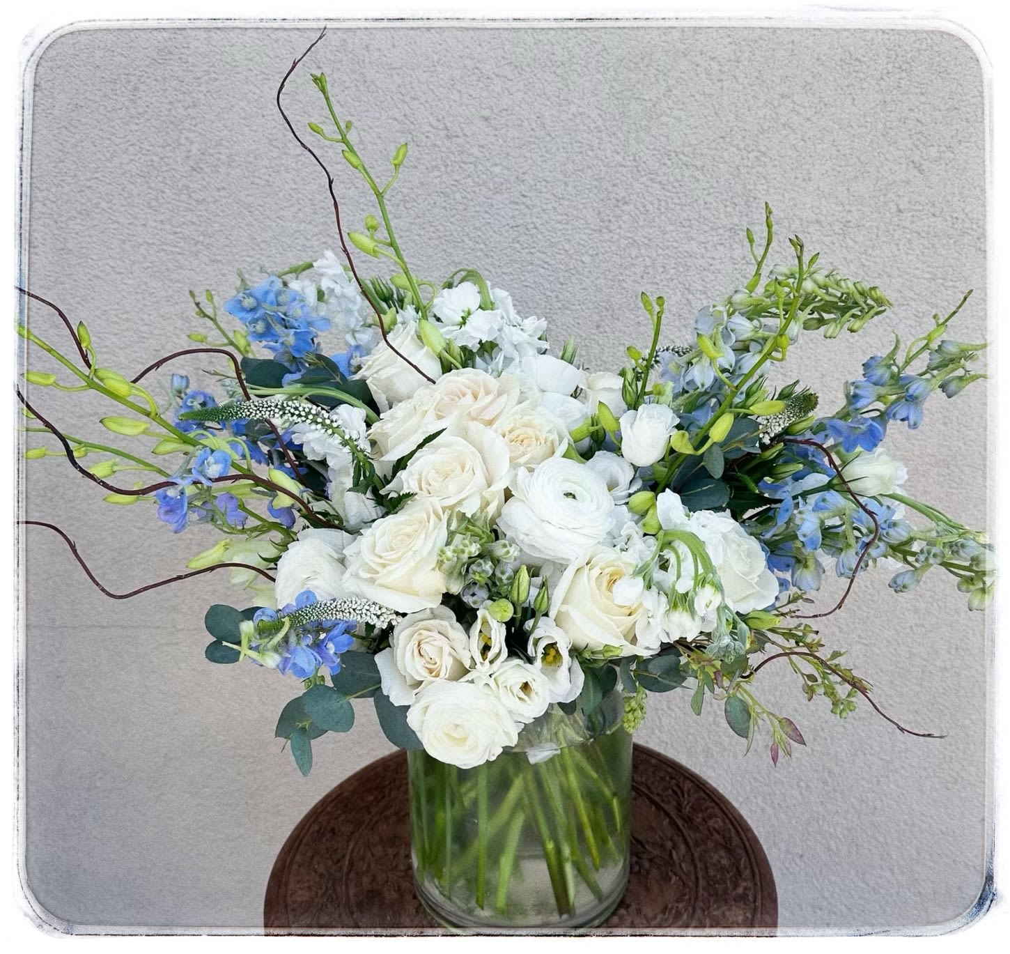 Blue Skies - This arrangement is a showstopper. It contains delphinium, ranunculus, roses, Lisi, stock, veronica and curly willow.