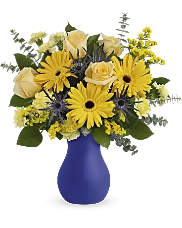 Glorious Morning Bouquet - As glorious as the sunrise, this golden mix of roses and gerberas in a bold blue frosted glass vase radiates joy. This bright arrangement features light yellow roses, yellow gerberas, blue eryngium, miniature yellow carnations, solidago, spiral eucalyptus and lemon leaf. Delivered in a Serendipity Glass Vase. Orientation: All-Around