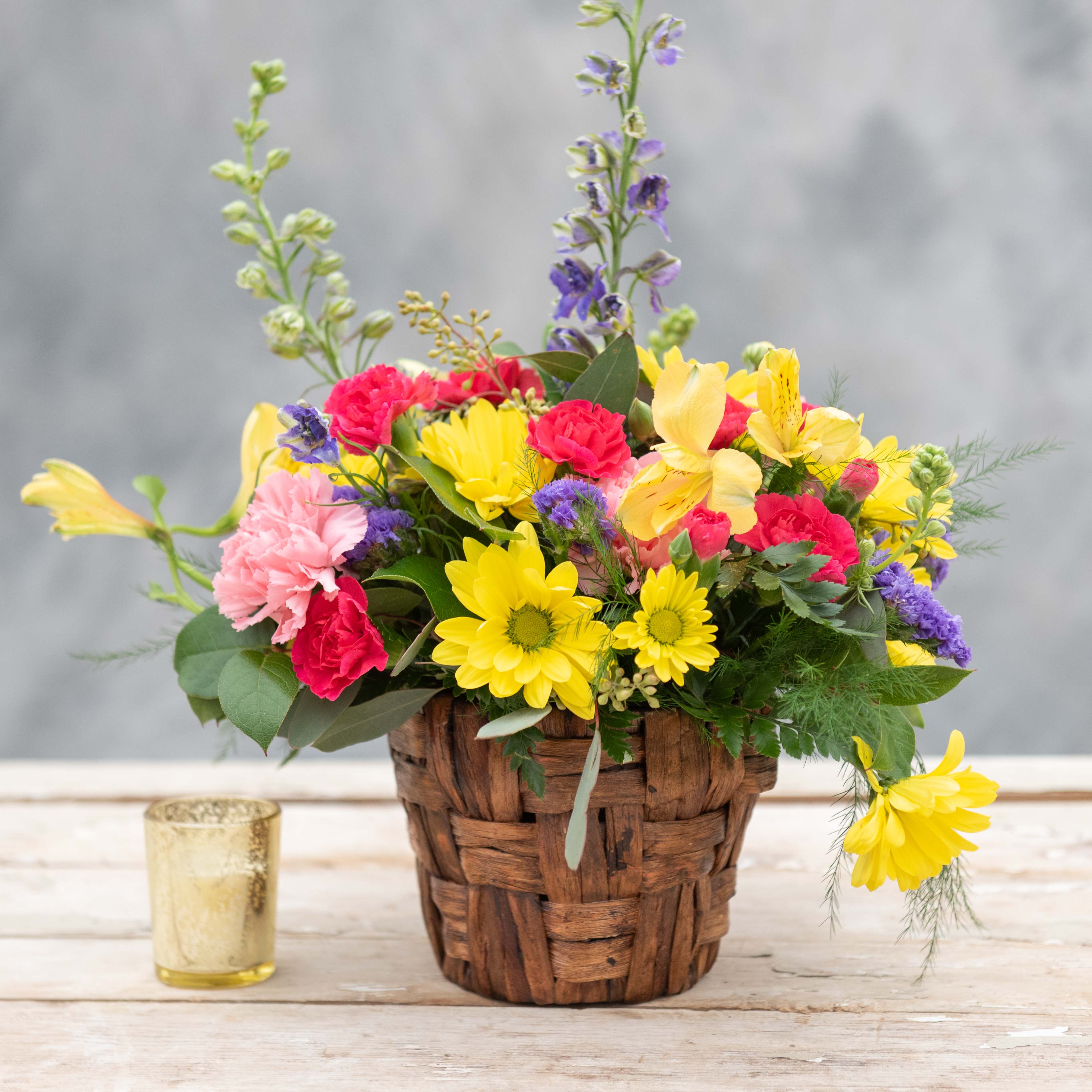 Basket of Blooms - The perfect touch of Spring color for any table in the house.  Enjoy this 5&quot; banana leaf basket bursting with long lasting flowers including hot pinks, yellows and purple -sure to brighten anyone's day.