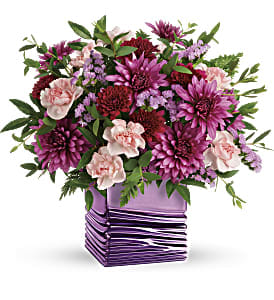 Liquid Lavender Bouquet  - Pour on the glam with this luxurious lavender cube! With its shimmering metallic finish and soothing wave detail, it's the perfect complement to a magnificent Mother's Day bouquet of lavender roses and rich, jewel-toned mums.  Lavender roses, light pink miniature carnations, burgundy cushion spray chrysanthemums, purple cushion spray chrysanthemums and lavender sinuata statice are arranged with huckleberry and parvifolia eucalyptus. Delivered in a Liquid Lavender cube.   Approximately 12 1/4&quot; W x 12 1/2&quot; H