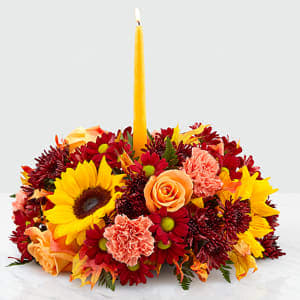 Giving Thanks Centerpiece Giving Thanks Centerpiece - Gather around a gorgeous centerpiece this harvest season. Our Giving Thanks Centerpiece is sure to add a touch of heartfelt warmth to any celebration with its collection of orange roses, sunflowers, glycerized oak leaves and orange carnations set around a golden taper candle. Whether you're a guest or the host, complete the table with an elegant centerpiece sure to brighten up the room