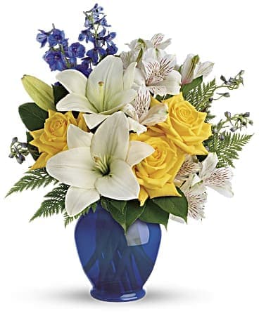 Oceanside Garden Bouquet - Like a sunny day at the shore, this bright bouquet invigorates and inspires! Radiant yellow roses, white lilies and blue delphinium are expertly arranged in our bold blue plastic ginger jar.  Sunny yellow roses, white asiatic lilies, white alstroemeria, and blue delphinium are arranged with leatherleaf fern and lemon leaf.