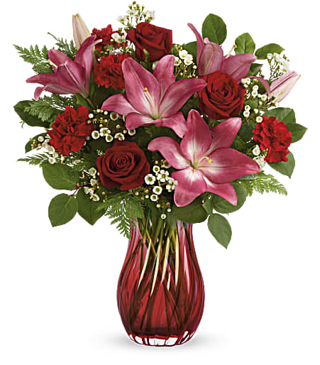 Enamored Elegance Bouquet  - Elegantly swirling glass, radiant red roses and pretty pink lilies are sure to make your enamored swoon! This elegant arrangement features red roses, pink asiatic lilies, red carnations, white waxflower, leatherleaf fern and lemon leaf. Delivered in Teleflora’s Love Conquers All vase. Approximately 18 3/4″ W x 19 3/4″ H