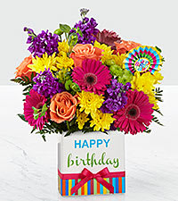 Birthday Brights Bouquet - The Birthday Brights Bouquet is a true celebration of color and life to surprise and delight your special recipient on their big day!   Hot pink gerbera daisies and orange roses take center stage surrounded by purple gilly flowers, yellow chrysanthemums, orange carnations, green button poms, bupleurum, and lush greens to create party perfect birthday display. Presented in a modern rectangular ceramic vase with colorful striping at the bottom, Happy Birthday&quot; lettering at the top, and a bright pink bow at the center, this unforgettable fresh flower arrangement is then accented with a striped happy birthday pick to create a fun and festive gift.  SUBSTITUTION POLICY – Always deliver the freshest flowers! Please note the bouquet pictured reflects our original design.  If the exact flowers or container in this arrangement are not available, we will create a beautiful bouquet with the freshest available flowers.