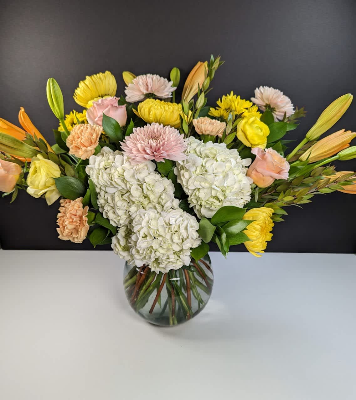 Lemon Cream Dream  - Experience the Dreamy Refreshment of Lemon Cream Dream Floral Arrangement  Lemon Cream Dream evokes the soft, creamy hues of lemon and blush, intertwined with bursts of vibrant orange and yellow, offering a dreamy and refreshing floral arrangement. This arrangement includes:  -White hydrangea -Orange lilies -Peach mums -Yellow mums -Yellow ranunculus -Orange carnations -Peach roses  Indulge in the serene beauty of Lemon Cream Dream, perfect for adding a touch of elegance and freshness to any space.
