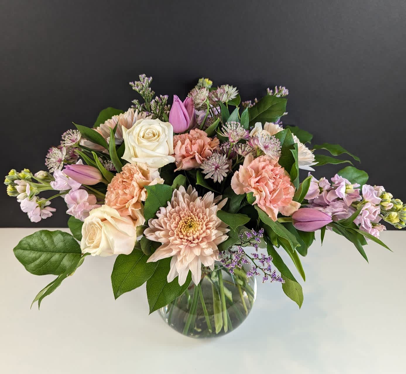 Pastel Dreams Flower Arrangement - Experience Serene Beauty with Our Soft Pastel Floral Arrangement  Indulge in the soft pastel palette of colors with this delightful arrangement. Featuring:  -Pastel pink chrysanthemums -Vintage pink carnations -Pastel purple stock -Blush roses -Lavender tulips -Purple astrantia -Purple misty  Embrace the serene beauty of these delicate hues, perfect for bringing a touch of elegance and tranquility to any space.