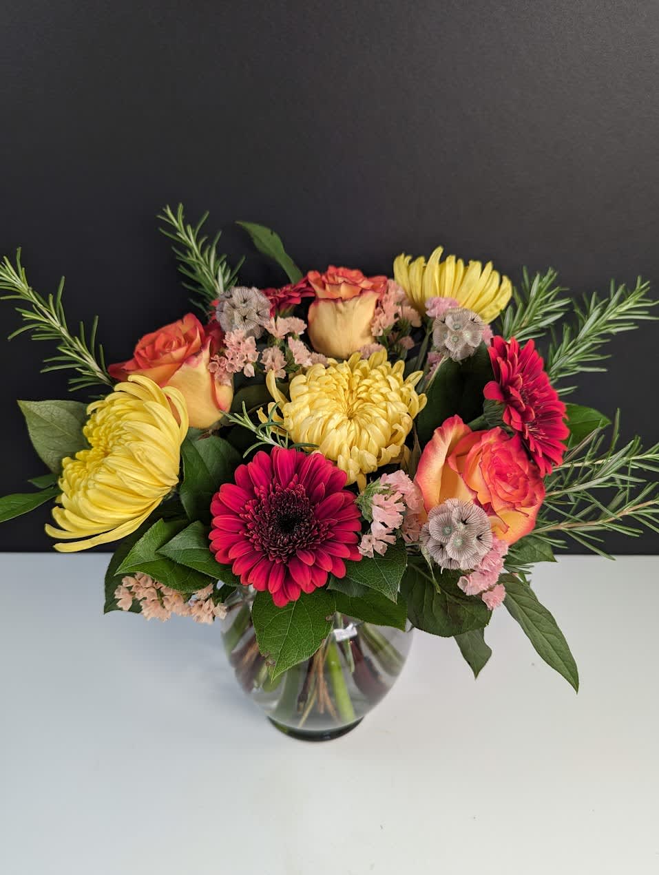 Golden Sunset Bouquet - Golden Sunset Bouquet  Witness the breathtaking hues of a summer sunset with our Golden Sunset Bouquet. This radiant arrangement showcases:  -Yellow mums -Orange and yellow roses -Burnt orange gerbera daisies  Each bloom embodies the warmth and splendor of a sunset, creating a captivating display that brightens any space with its vibrant colors. Embrace the beauty of nature's golden hour with the Golden Sunset Bouquet, perfect for adding a touch of joy and elegance to any occasion.