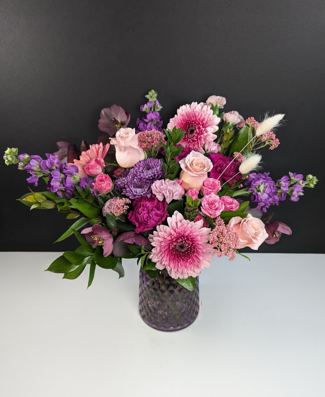 Sweet Pea Symphony  - Experience the Harmony of Spring with Sweet Pea Symphony Floral Arrangement  Sweet Pea Symphony evokes the harmonious charm of springtime with its delicate blend of pink and purple blooms, creating a melody of sweetness and elegance. This arrangement features:  -Pink gerbera daisies -Dark purple helleborus -Dark purple stock -Pink spray roses -Purple mums -Peach roses -Magenta carnations -Lavender mini carnations  Indulge in the beauty of spring with this enchanting arrangement, perfect for adding a touch of elegance to any occasion.  
