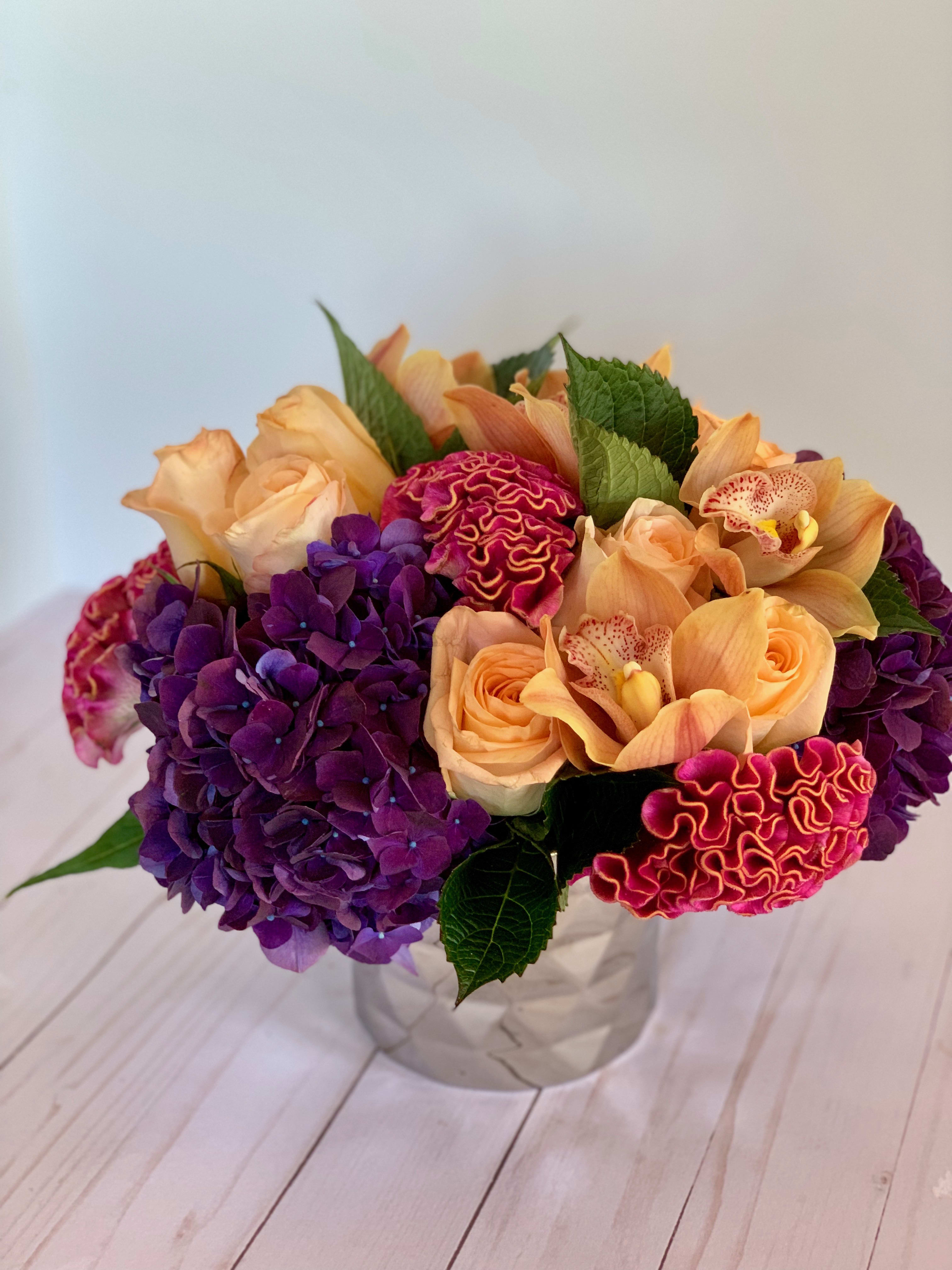 Peek of Peach - Vibrant, tight floral arrangement of dutch varieties in deep purple, fuschia, green and a pop of peach to bring it all together.  Stunning!