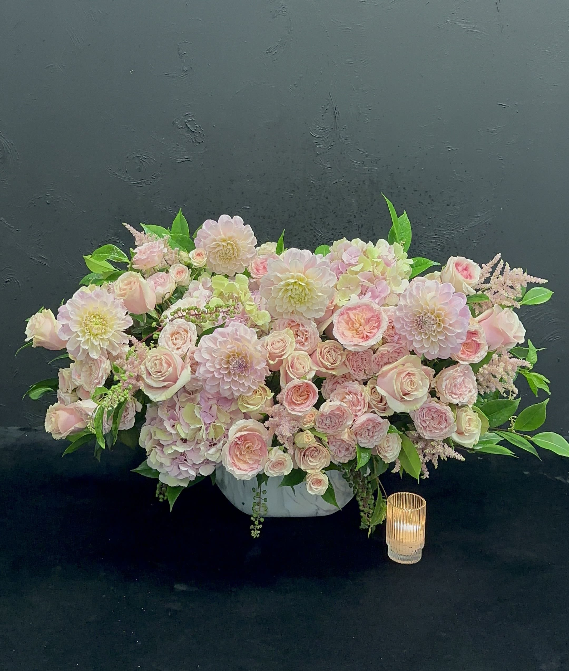 Delicate Harmony - This lovely arrangement features a delightful mix of pastel dahlias, garden roses, and spray roses, creating a soft and romantic palette. The dahlias, with their lush, layered petals, provide a beautiful focal point, while the garden roses add a timeless elegance with their fragrant blooms. Interspersed throughout are charming spray roses, adding a touch of whimsy and fullness. The combination of these flowers, in gentle hues of blush, peach, and cream, creates a serene and uplifting display, perfect for celebrations, weddings, or simply brightening up any space.    