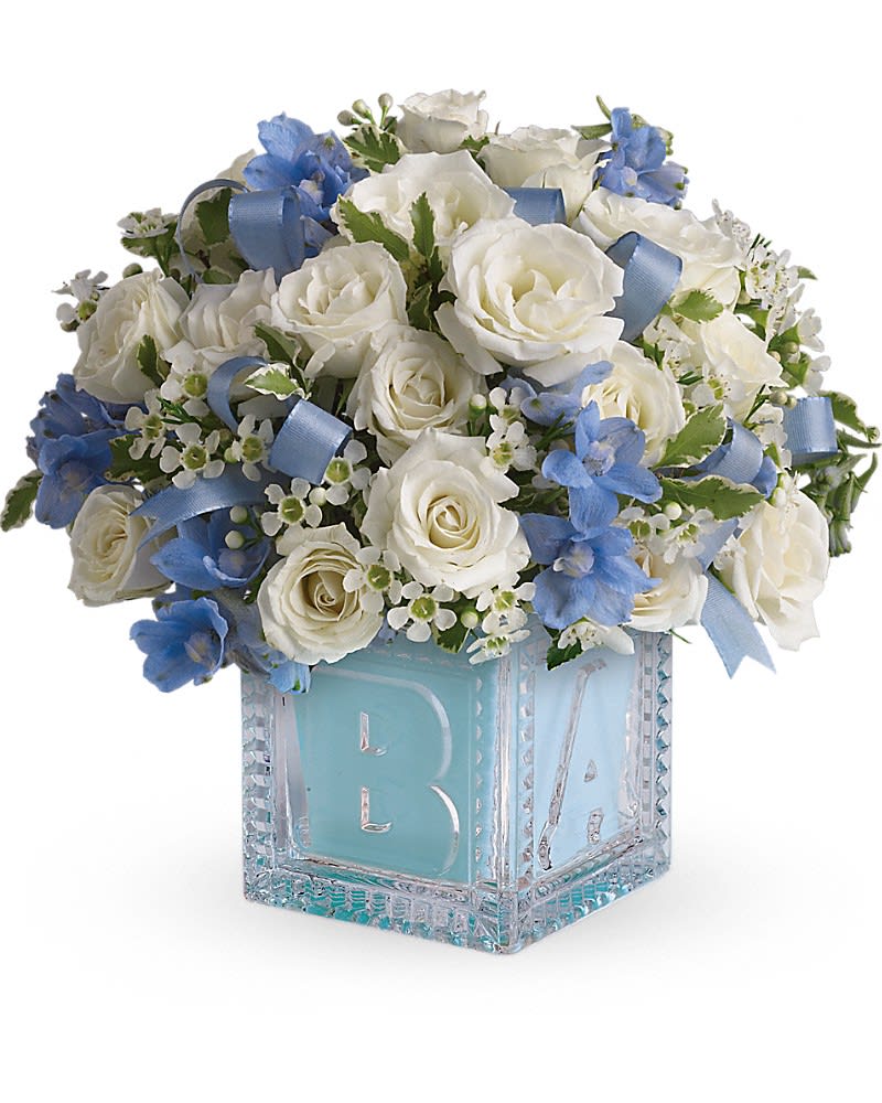 Baby's First Block by Teleflora - Blue - Celebrate the coolest baby boy on the block's arrival with this charming glass baby block that arrives chock full of pretty flowers. Perfect for baby showers too! The glass block will make an adorable display piece for years! Dazzling white spray roses light blue delphinium white waxflower and light blue organza ribbon are delivered in a clear baby block with a light blue liner. One great delivery deserves another don't you think?