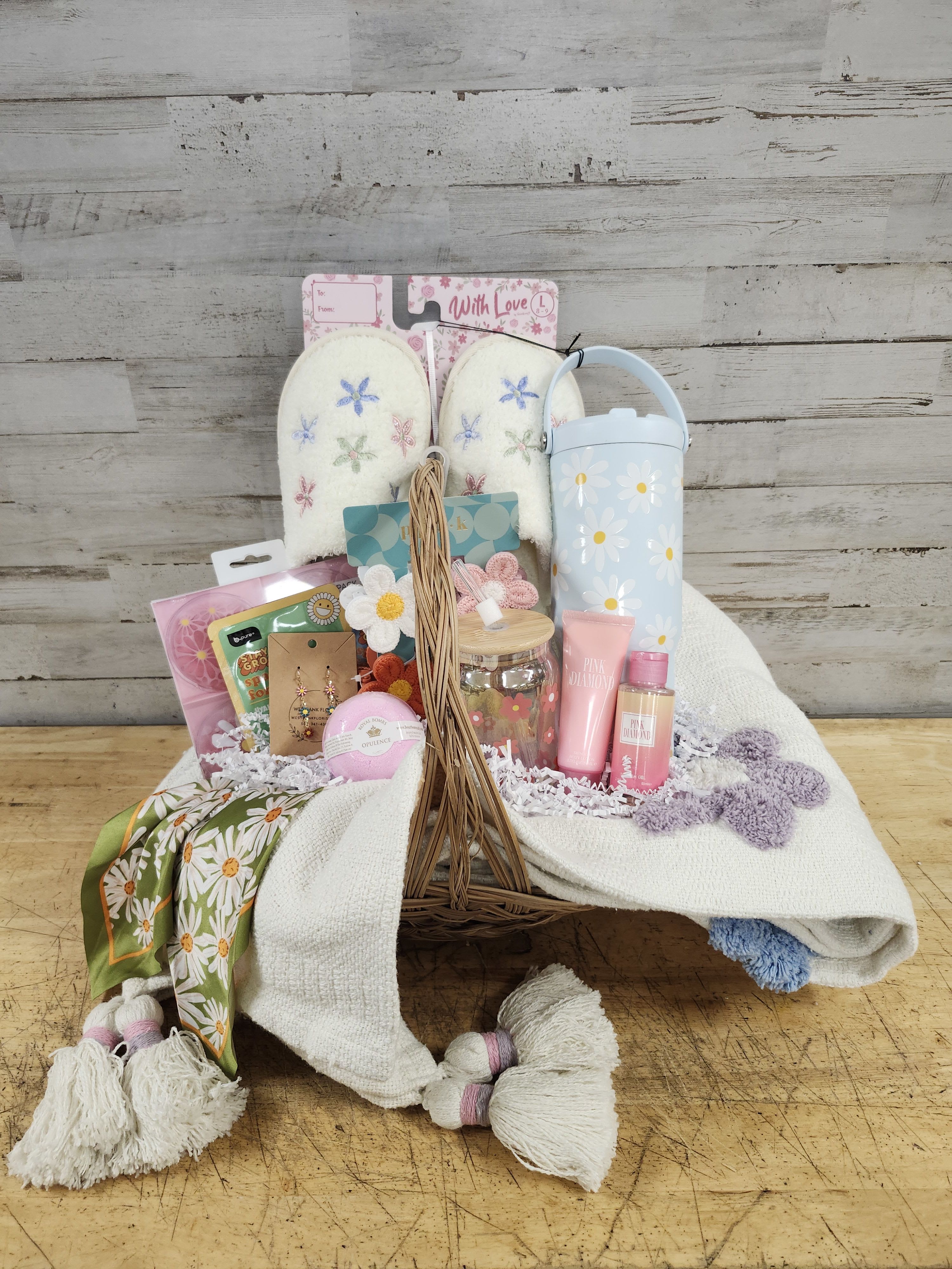 Crazy for Daisy - $190 - A cute and fun gift sure to please those of any age this basket features:  Premium Knit Blanket with Tassels Daisy Shaped Hair Clips (4 Set) Hot/Cold Eye Pads Glass Cup With Straw Insulated Hydropeak Waterbottle Dangly Daisy Earrings Cozy Slippers Hair Tie with Bow Strings Pink Diamond Spa Set Bourbon Royalty Bath Bomb   