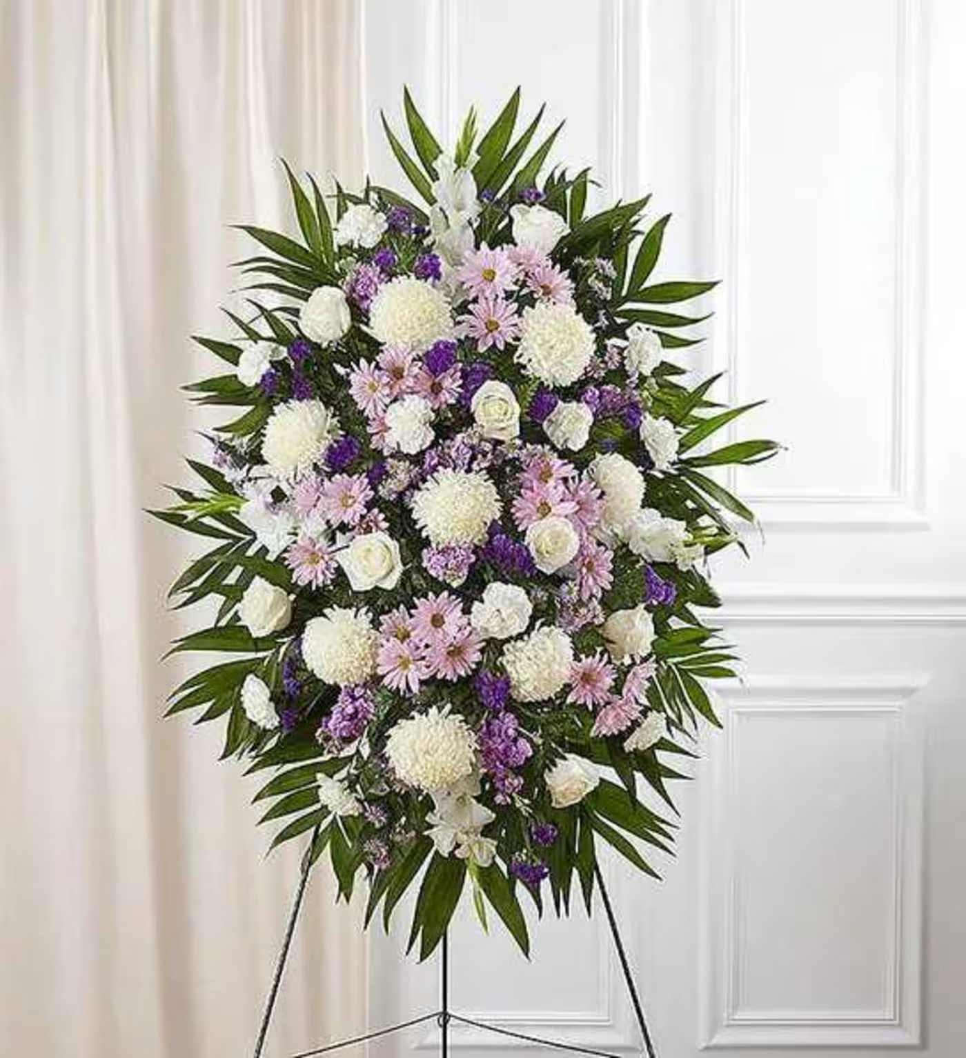 Lavender And White Funeral Standing Spray - When words alone cannot convey the feelings in your heart, flowers can provide a meaningful and profound statement. Our impressive standing spray arrangement is meticulously handcrafted by expert local florists with soothing lavender and white blooms for a lush, full presentation, presenting an elegant and memorable tribute.  Standing spray arrangement with lavender daisy poms, stock and monte casino; white roses, Oriental lilies, football mums, gladiola and carnations; purple statice; accented with soft, lush greenery Large measures approximately 56&quot;H x 38&quot;L without stand Medium measures approximately 46&quot;H x 34&quot;L without stand Small measures approximately 42&quot;H x 30&quot;L without stand Arrives on an easel Appropriate for the funeral home or gravesite Our florists hand-design each arrangement, so colors and varieties may vary due to local availability