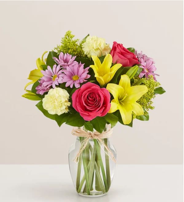 Fields of Europe® for Mom - Mom is in for a beautiful surprise! Our best-selling Mother’s Day arrangement is designed in the same tradition as the hand-tied bouquets found in European flower markets. A vibrant mix of blooms inside a glass vase tied with raffia, it’s a gift that delights with old-world charm and style.  All-around arrangement with hot pink roses; yellow Asiatic lilies and carnations; lavender daisy poms; solidago; accented with assorted greenery Artistically designed in clear glass vase tied with raffia; measures 8&quot;H Premium arrangement measures approximately 18&quot;H x 14&quot;W Deluxe arrangement measures approximately 17&quot;H x 13&quot;W Standard arrangement measures approximately 16&quot;H x 12&quot;W Our florists hand-design each arrangement, so colors, varieties and container may vary due to local availability To ensure lasting beauty, Asiatic lilies may arrive in bud form and will fully bloom over the next few days