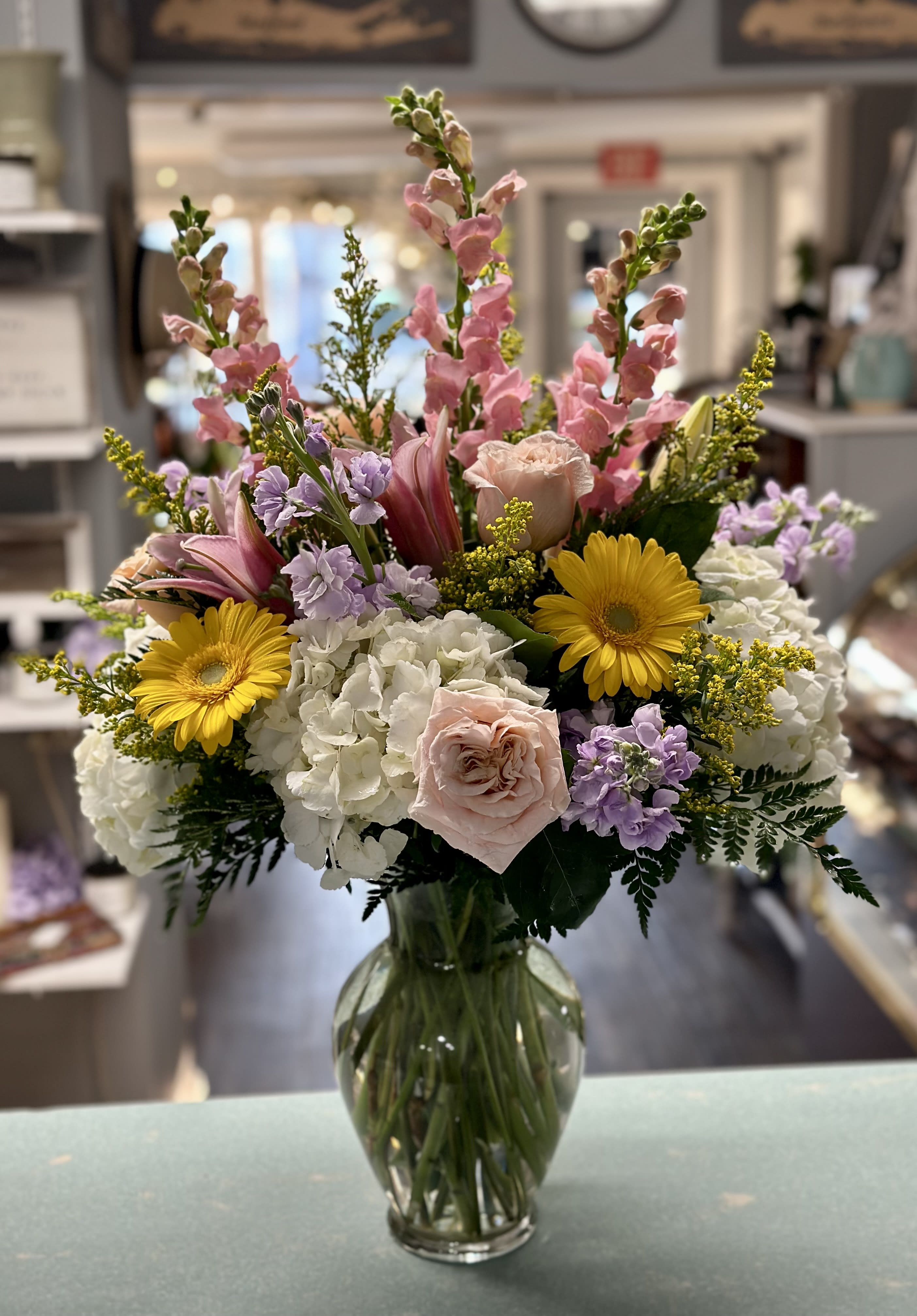 Garden of Gratitude Garden of Gratitude - White hydrangea, pink oriental lily, pink snapdragon, lavender stock, yellow gerbera daisy, peach rose, solidago, greenery in a 11'' clear classic urn vase