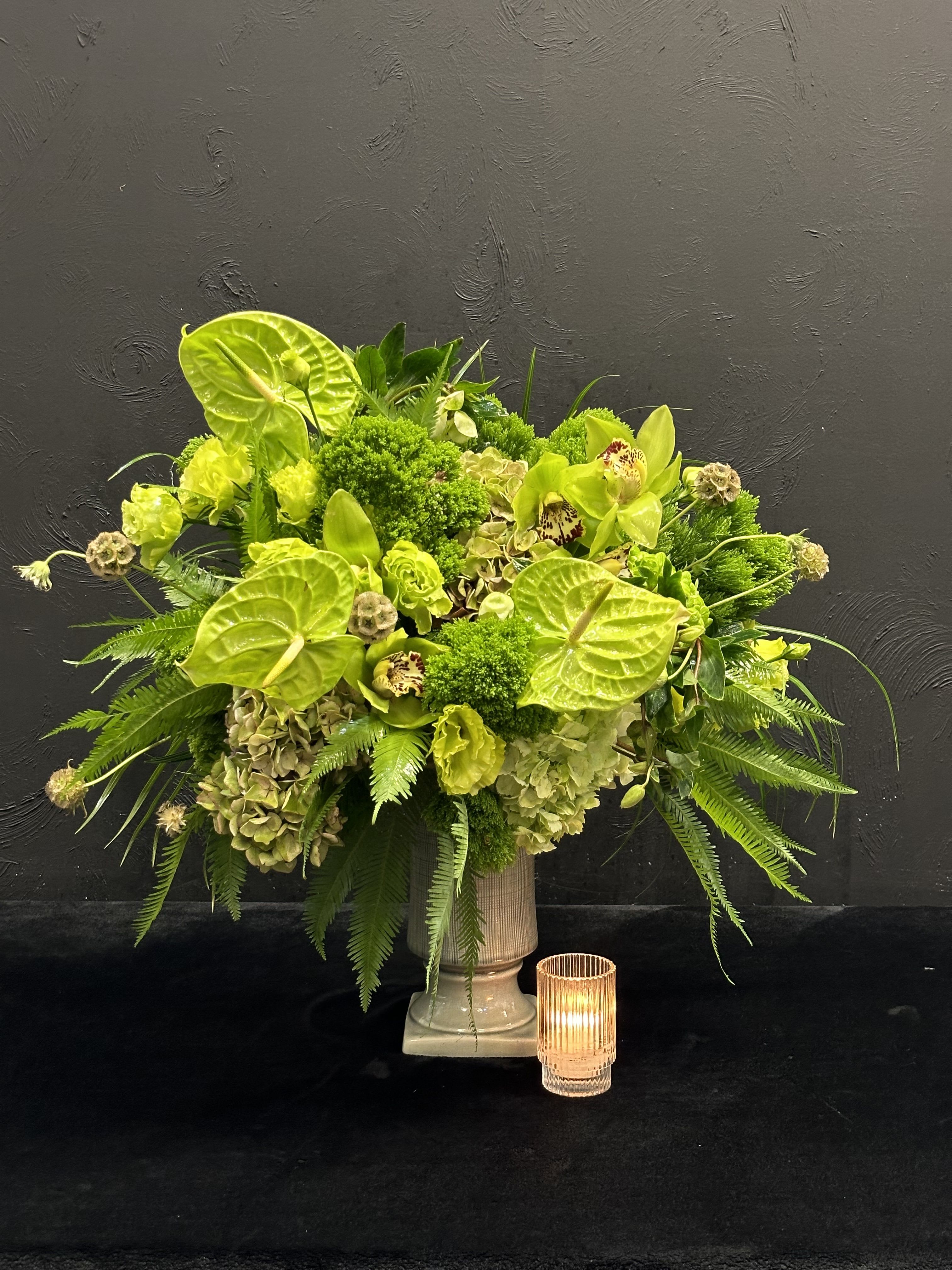 Green Enchantment - This striking arrangement features a vibrant mix of green flowers, creating a lush and refreshing display. Elegant orchids add a touch of sophistication with their unique shapes, while the bold anthuriums provide a glossy finish that catches the eye. Delicate lisianthes contribute a soft, romantic texture, and the hydrangeas bring volume and depth to the composition. Together, these green blooms create a serene and harmonious atmosphere, perfect for adding a touch of nature’s beauty to any space.    
