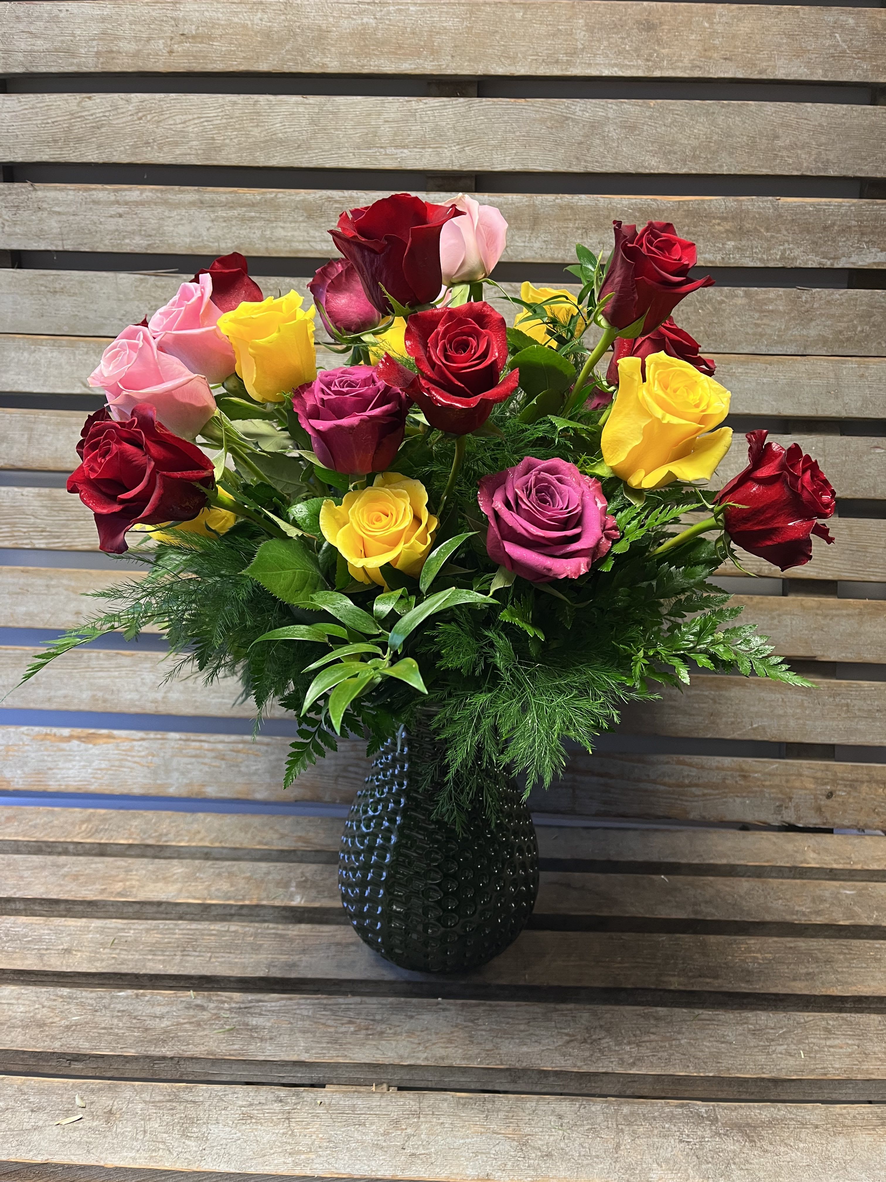 2 dozen assorted roses vases  - Two dozen assorted colored roses, arranged with different textures of greens in a green hob knob vase. 
