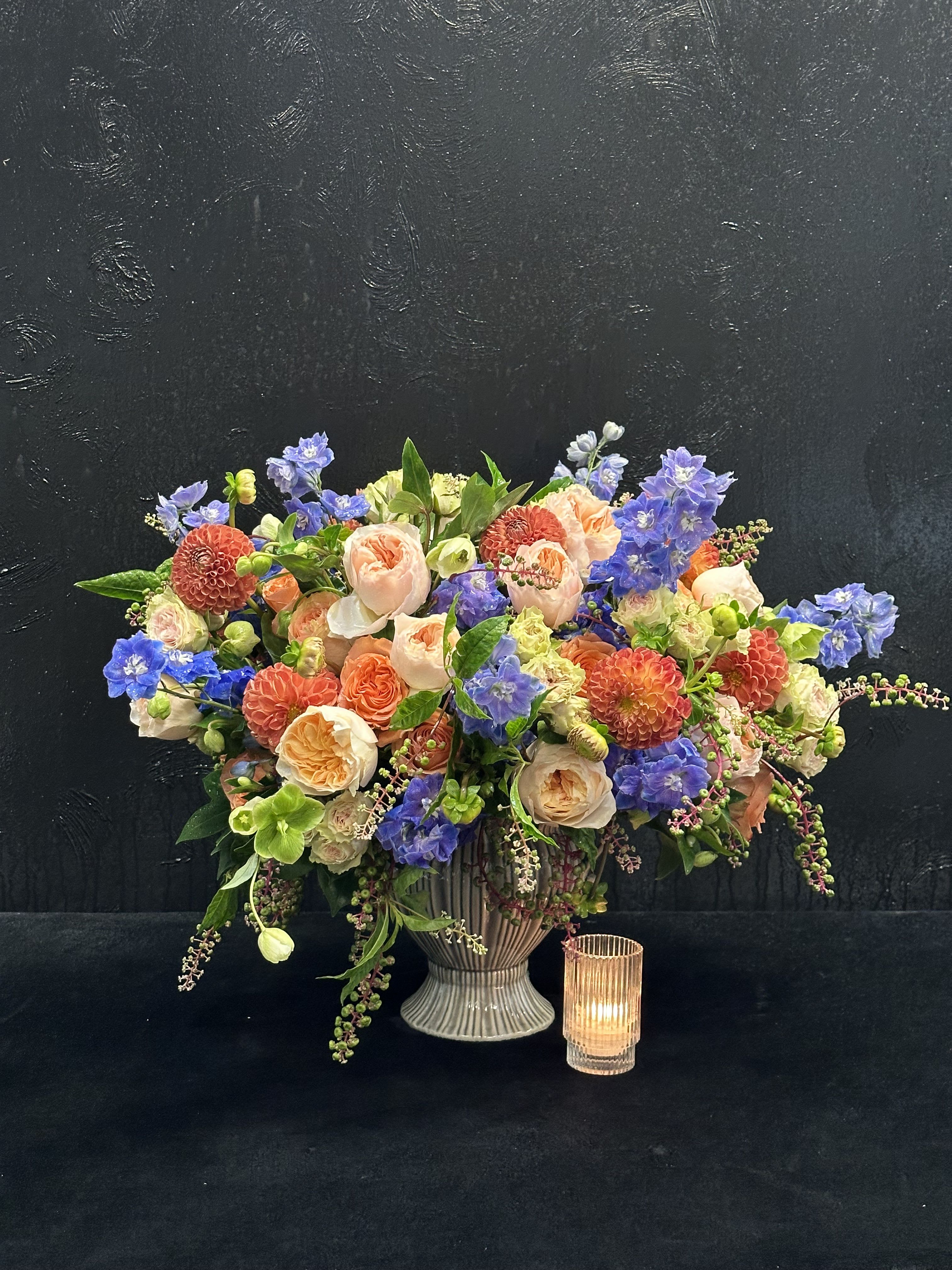 Sunset Harmony - Brighten your space with Sunset Harmony, a vibrant arrangement of peach dahlias, orange spray roses, and blue delphinium. This cheerful composition captures the warmth of a sunset, making it perfect for celebrations or as a lively accent in your home. Let the joyful colors of Sunset Harmony bring charm and warmth to any occasion.  