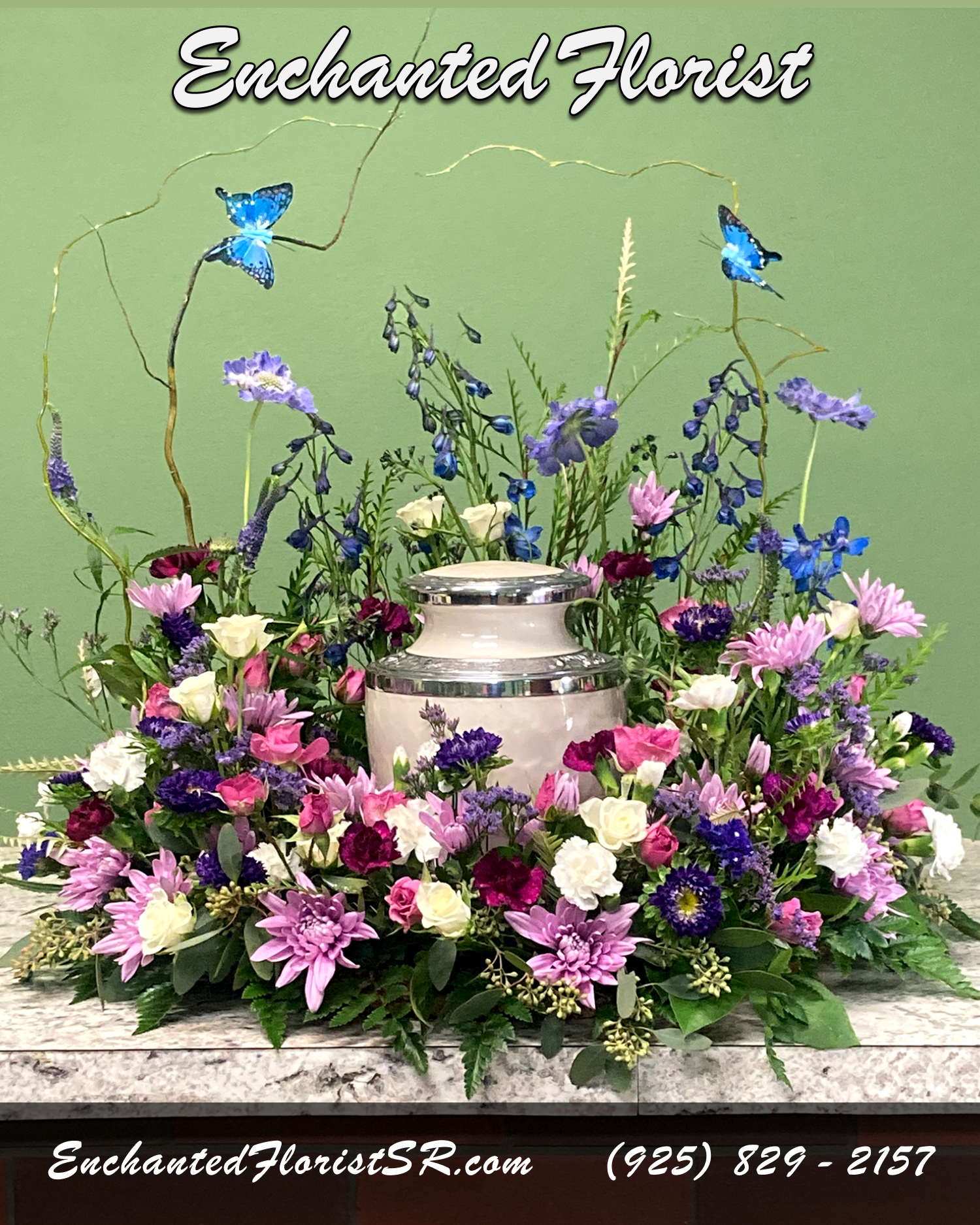 Twilight - Urn Wreath - A heartfelt urn wreath that honors cherished memories with grace, showcasing an elegant palette of purple, lavender, and blue. Meticulously arranged to evoke the beauty of nature.  Featuring chrysanthemums, scabiosas, carnations, asters, spray roses, veronica, and thistle, this tribute is accented with statice, grevillea, and curly willow strands adorned with decorative blue butterflies for a touch of enchantment.  Urn wreaths are traditionally ordered by immediate family members, and are sent to reception sites before the ceremony begins. Intended to be set on a flat surface, with an urn or framed photo placed within the wreath center, creating a loving tribute and providing solace and comfort during times of loss.  Please Note: Urn wreath does not include urn.  Approximate Dimensions: 30&quot; Wreath Height 28&quot; Wreath Diameter