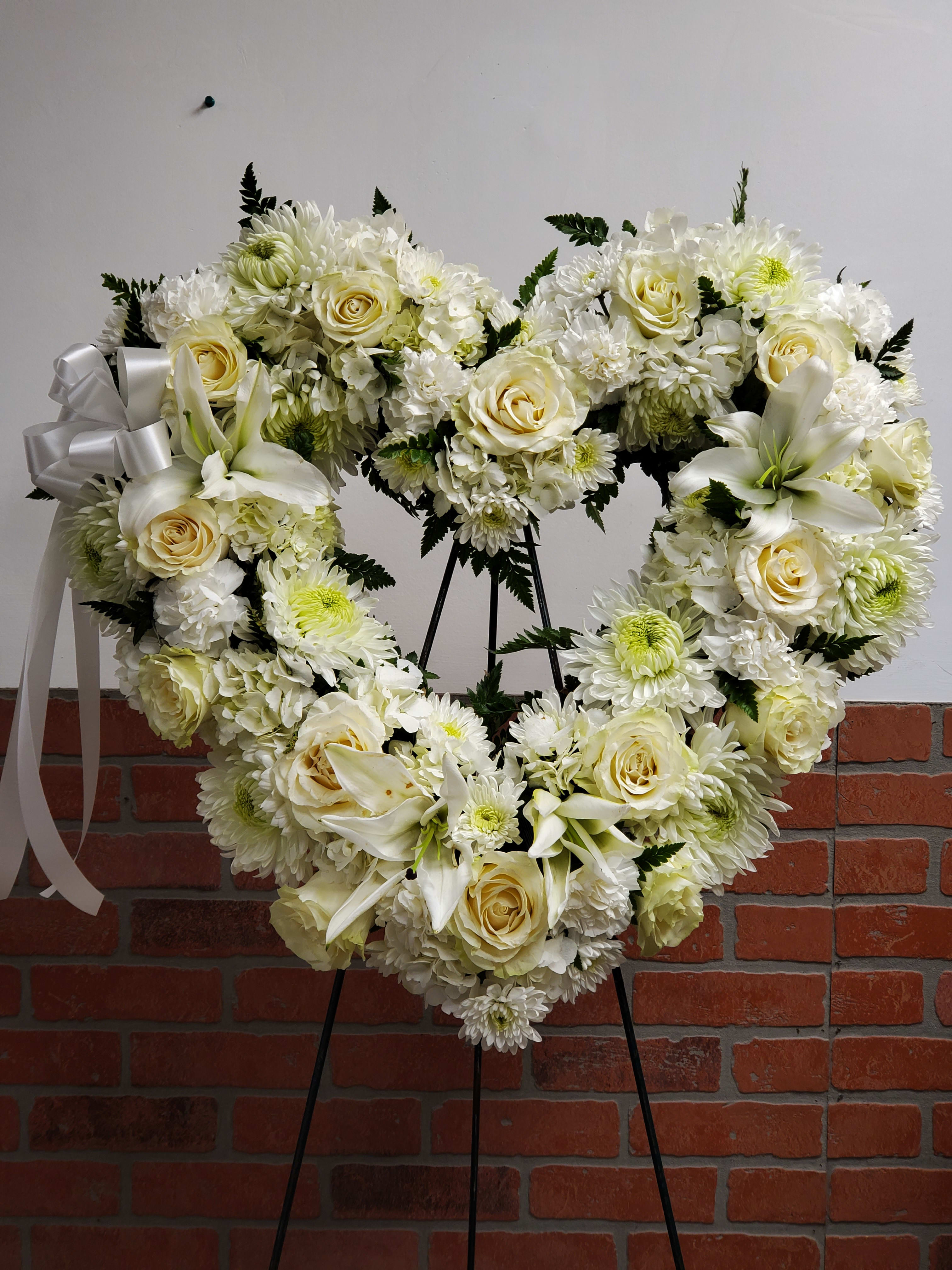 Love in our Hearts by Manny - An all white tribute, this heart shaped easel shows your everlasting love. Featuring a variety of white flowers and greenery, this heart with a trail of ivy compliments the beauty of life. 