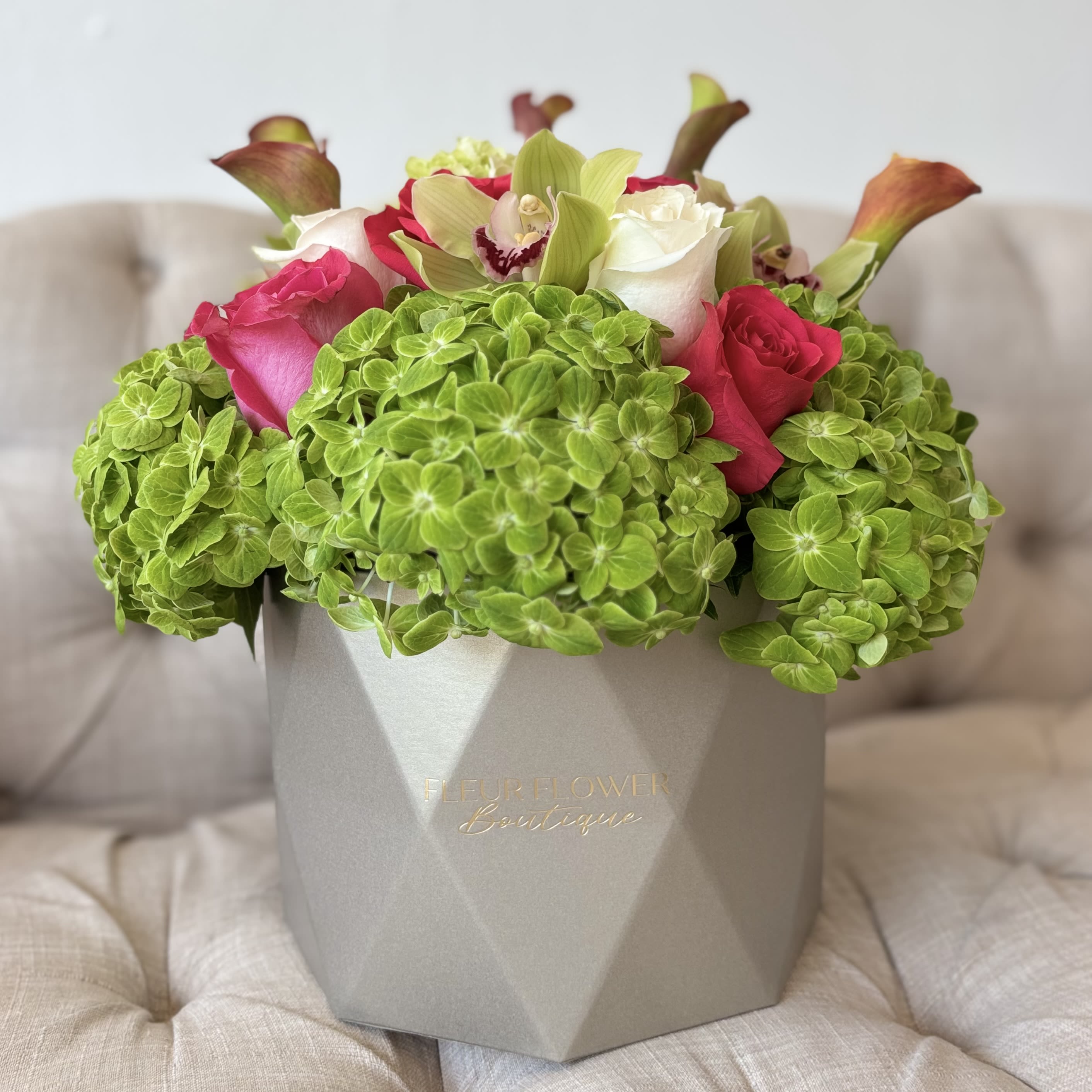 Serena - Serena is a striking floral arrangement that includes vibrant&nbsp; orchids,calas,&nbsp; white roses and green hydrangeas. Presented in a 9x7 inch geometric vase. This arrangement is perfect for adding a touch of color and sophistication to any space&nbsp;