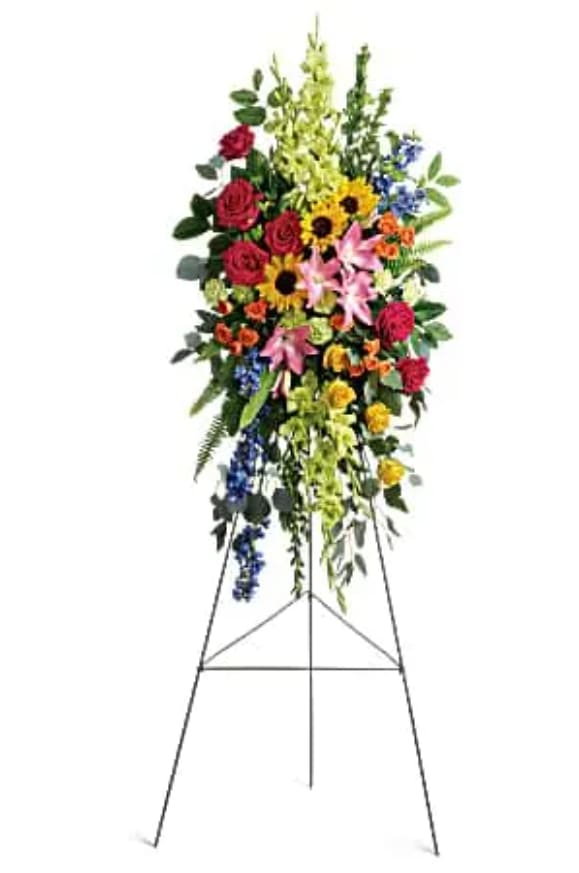 Love Lives On Spray - Bursting with joy, this radiant spray of rainbow blooms is an exuberant tribute to never-ending love. This spray features hot pink roses, yellow roses, orange spray roses, pink asiatic lilies, green gladioli, green carnations, medium yellow sunflowers, blue delphinium, bupleurum, myrtle, sword fern, silver dollar eucalyptus, and lemon leaf. Delivered on a wire easel.