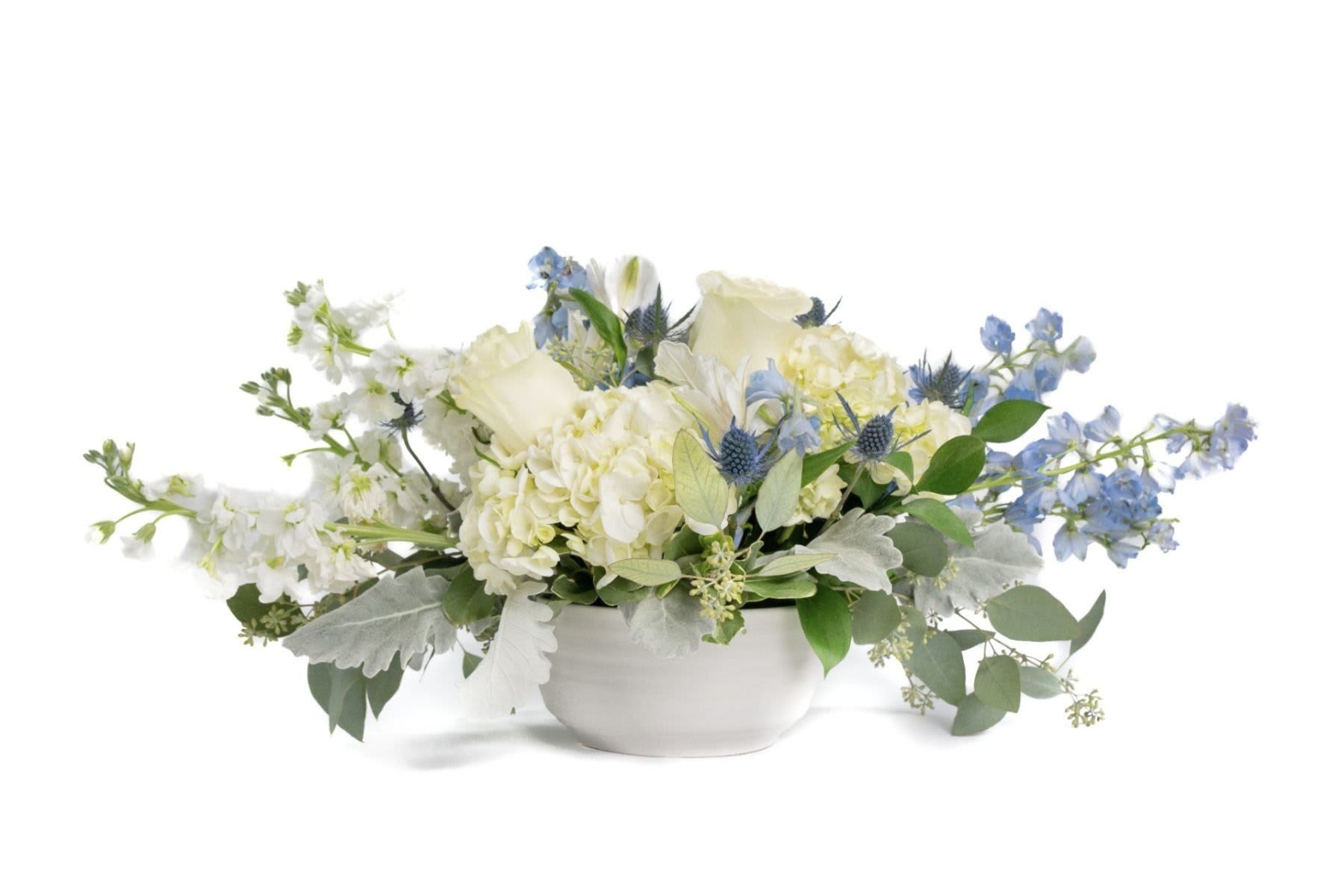 New Year Blessings New Year Blessings - This beautiful centerpiece will truly bring joy, comfort and happiness for the new year or any occasion. A fresh gathering of lush white hydrangeas, cream roses, beautiful blue delphinium with touches of alstroemeria and thistle.