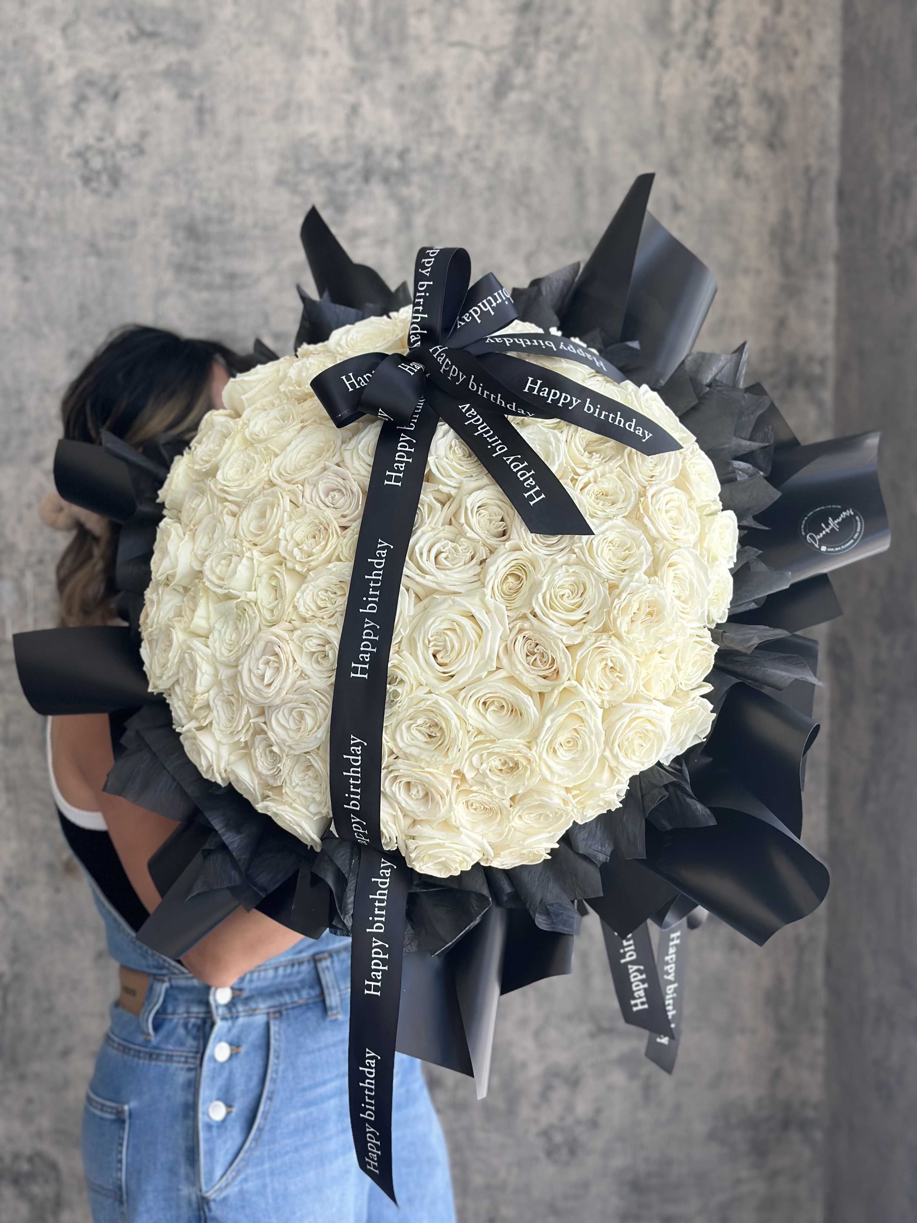 Noir Blanc - A Chic bouquet with 99 premium long stem white roses, fancy black wrap. Birthday bow ribbon. Photo is Deluxe size. Standard is 50 roses.