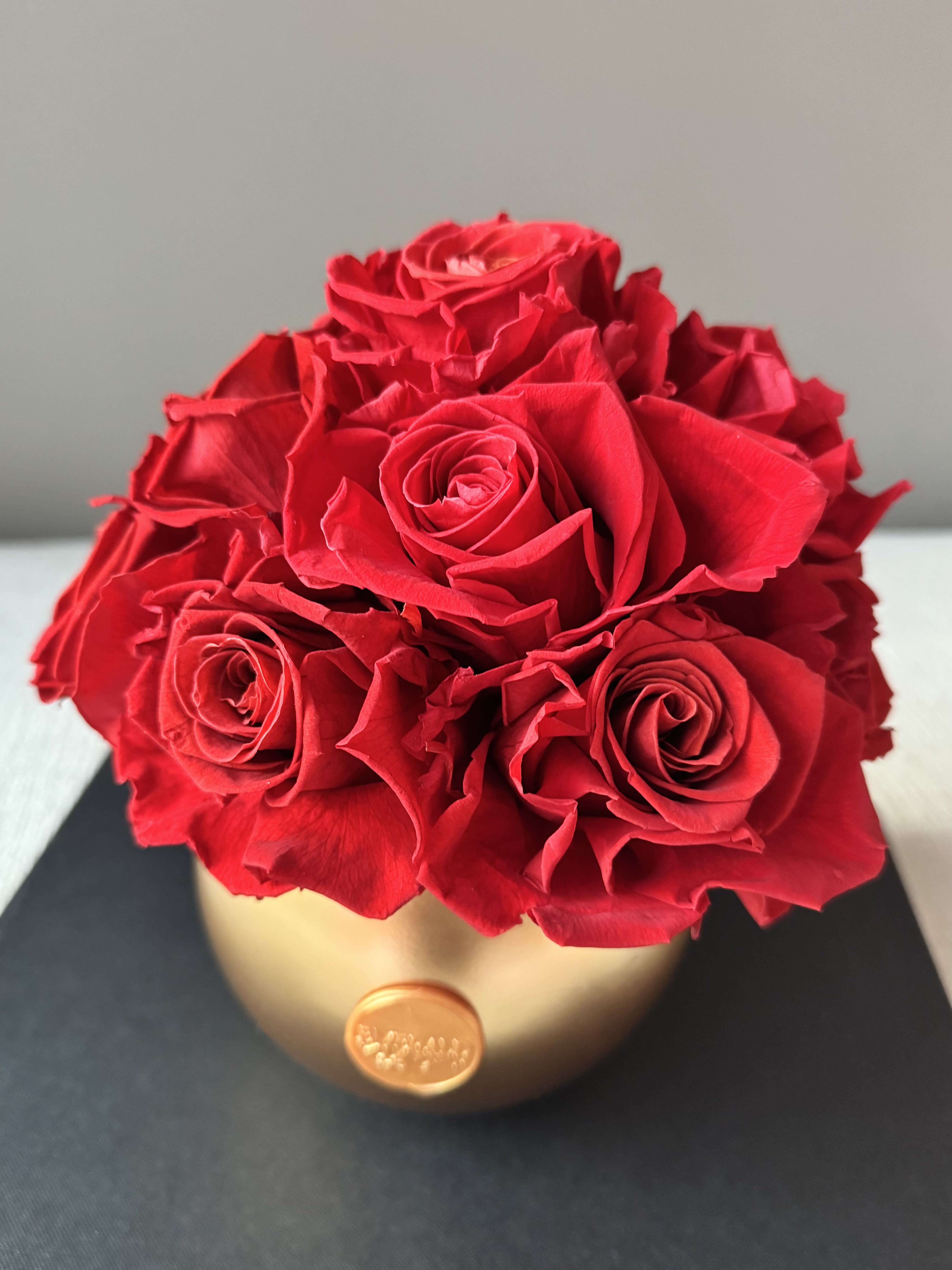 Eternelle Rouge – Gold Luxe Orbe - A statement of timeless romance, Eternelle Rouge – Gold Luxe Orb embodies passion and luxury in its purest form. Featuring a dozen meticulously preserved deep red roses, this arrangement is artfully designed in a Gold Luxe Orb vase—a modern, sculptural piece with a smooth, rounded silhouette that exudes elegance and sophistication. Each bloom is carefully selected to maintain its beauty for years, making it the perfect symbol of enduring love and refined taste.  Dimensions: 8in W x 9in H  Care Tips: To preserve the beauty of your Eternelle arrangement, keep it in a cool, dry place away from direct sunlight, humidity, and heat sources. No watering or maintenance is required—simply enjoy its everlasting elegance. Avoid touching the roses frequently to maintain their delicate texture, and use a soft brush or gentle air duster to remove any dust from the petals or vase. With proper care, your arrangement will remain a stunning display of luxury for years to come.  Availability: Each Eternelle arrangement is handcrafted with the utmost care. If this arrangement is marked SOLD OUT, you can place an order to reserve yours, and we will provide the earliest available delivery date. Please allow approximately one week for restocking and fulfillment. Thank you for your patience as we create your exquisite arrangement. 