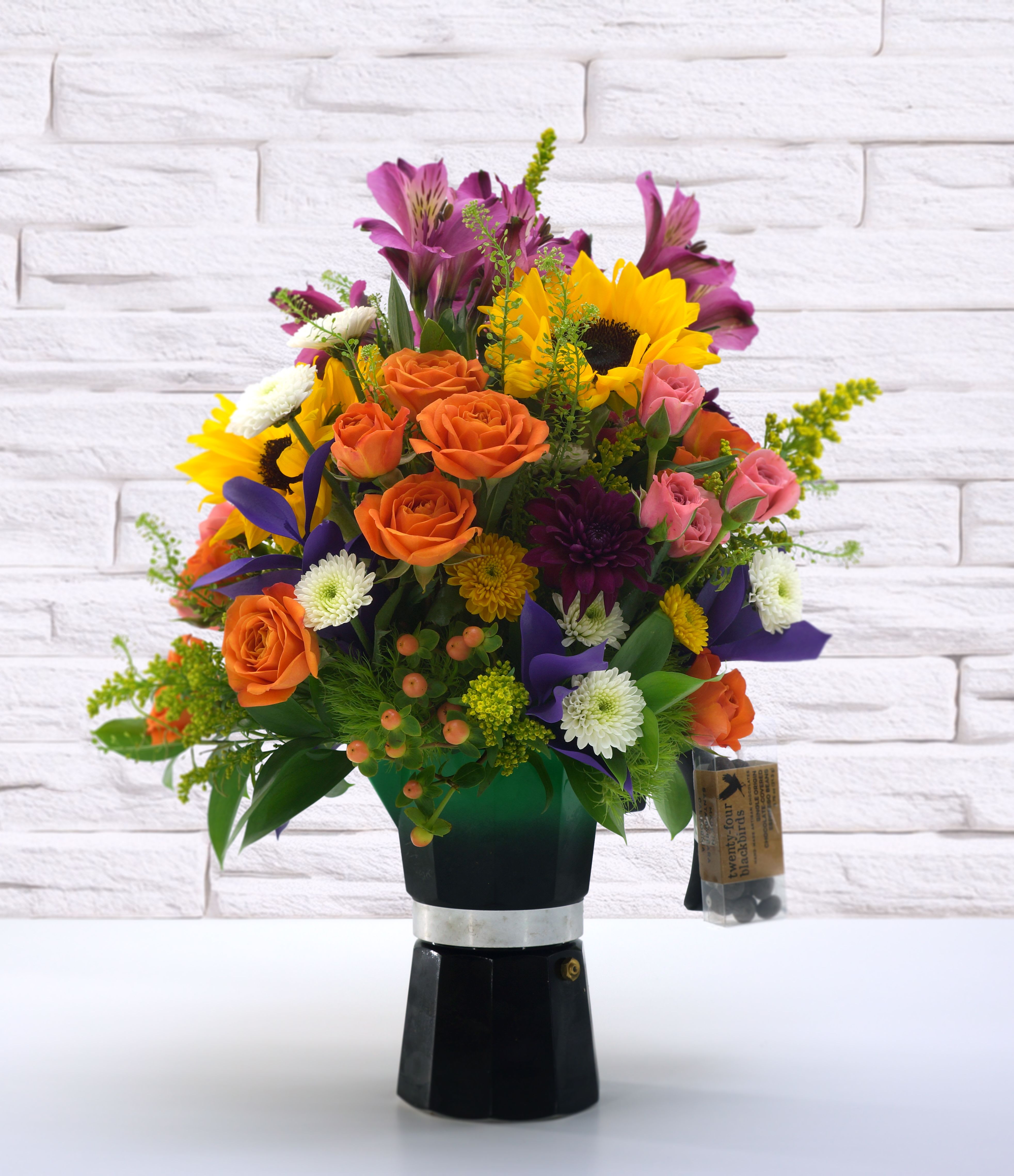Café Jewel | With Premium Chocolate Covered Espresso Beans - Our Café Jewel bouquet focuses on a jewel-toned color palette of sunflowers, roses, buttons, and dianthus. All inside a 7&quot; tall solid green and black espresso maker with an elegant wooden handle. The espresso maker is fully functional and serves up to 5 cups.  Included are hand-made artisan chocolate-covered espresso beans. The coffee roaster Low Pigeons’ Malawi AAA espresso beans with 75% Öko Caribe chocolate. The combo is out of this world in both deep coffee flavor and delicious dark chocolate notes, with hints of fruit and spice. For reference, the 21g size is equal to a healthy double shot of espresso.  Ingredients: Organic Dominican Cocoa Beans, Green Cane Certified Cane Sugar, Espresso Beans.  Exclusive to local delivery. Limited quantity.