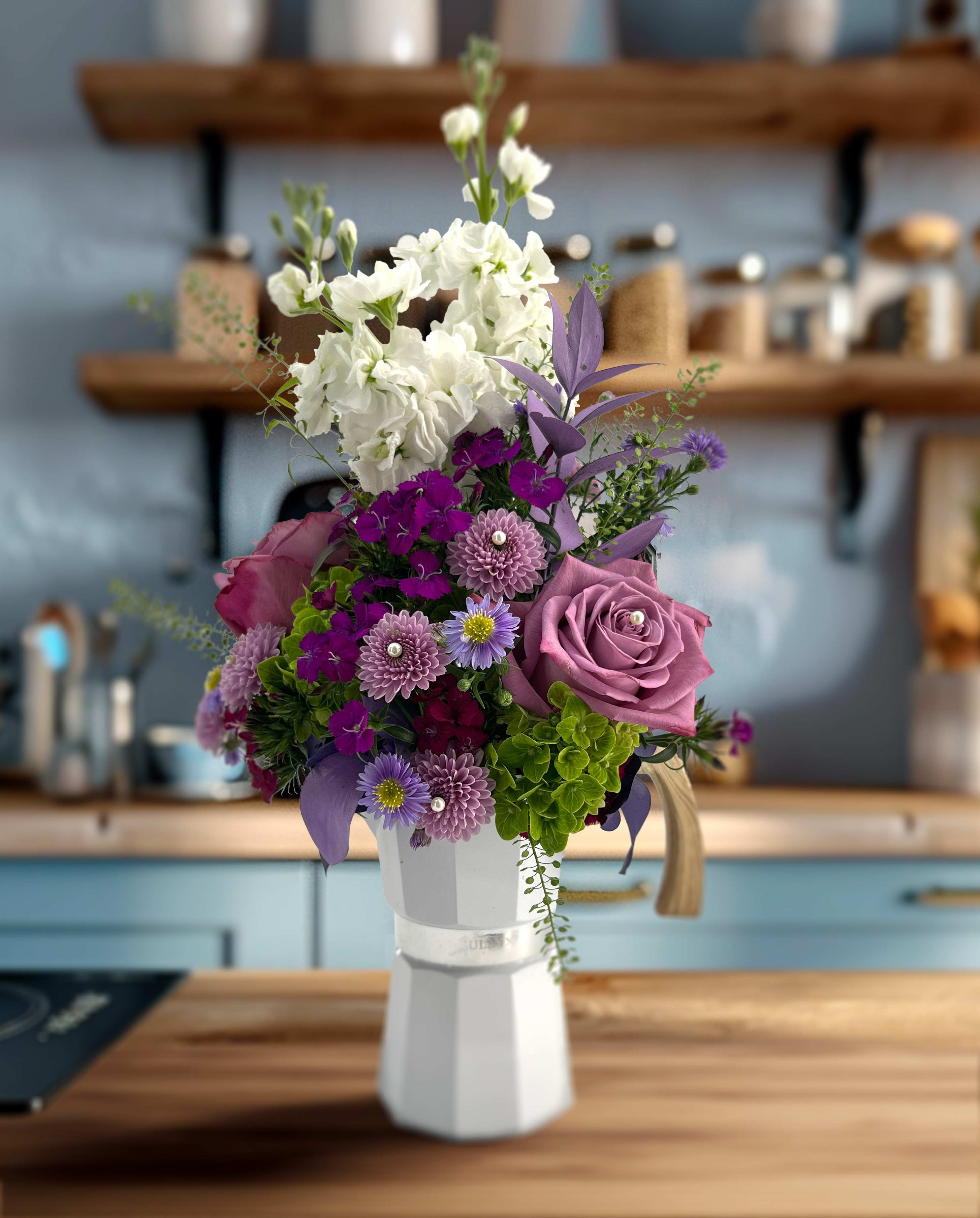 Café Lavender | With Premium Chocolate Covered Espresso Beans - We've put together something special for those who love their café. This bouquet is composed of roses, mums, dianthus, hydrangeas, ruscus and is adorned with delicate pearls. All inside a 7&quot; tall solid white espresso maker with an elegant wooden handle. The espresso maker is fully functional and serves up to 5 cups. Limited quantity.  Included are hand-made artisan chocolate-covered espresso beans. The coffee roaster Low Pigeons’ Malawi AAA espresso beans with 75% Öko Caribe chocolate. The combo is out of this world in both deep coffee flavor and delicious dark chocolate notes, with hints of fruit and spice. For reference, the 21g size is equal to a healthy double shot of espresso.  Ingredients: Organic Dominican Cocoa Beans, Green Cane Certified Cane Sugar, Espresso Beans.  Exclusive to local delivery. Limited quantity. 