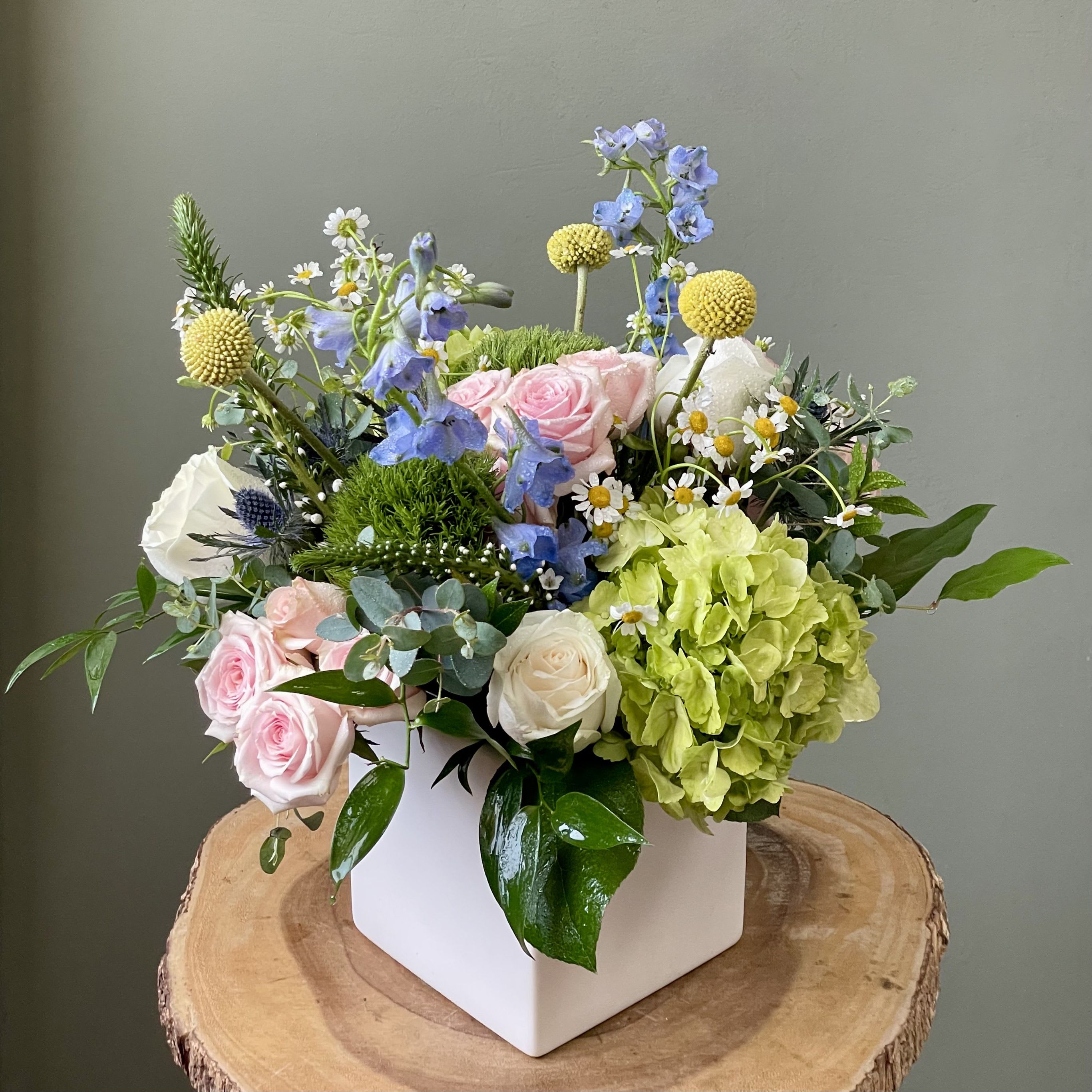 Spring Kisses (SF552) - Delight in the charm of spring with this enchanting arrangement of pastel blooms, artfully arranged in a sleek white ceramic square vase. Perfect for brightening any space and spreading the joy of the season! 