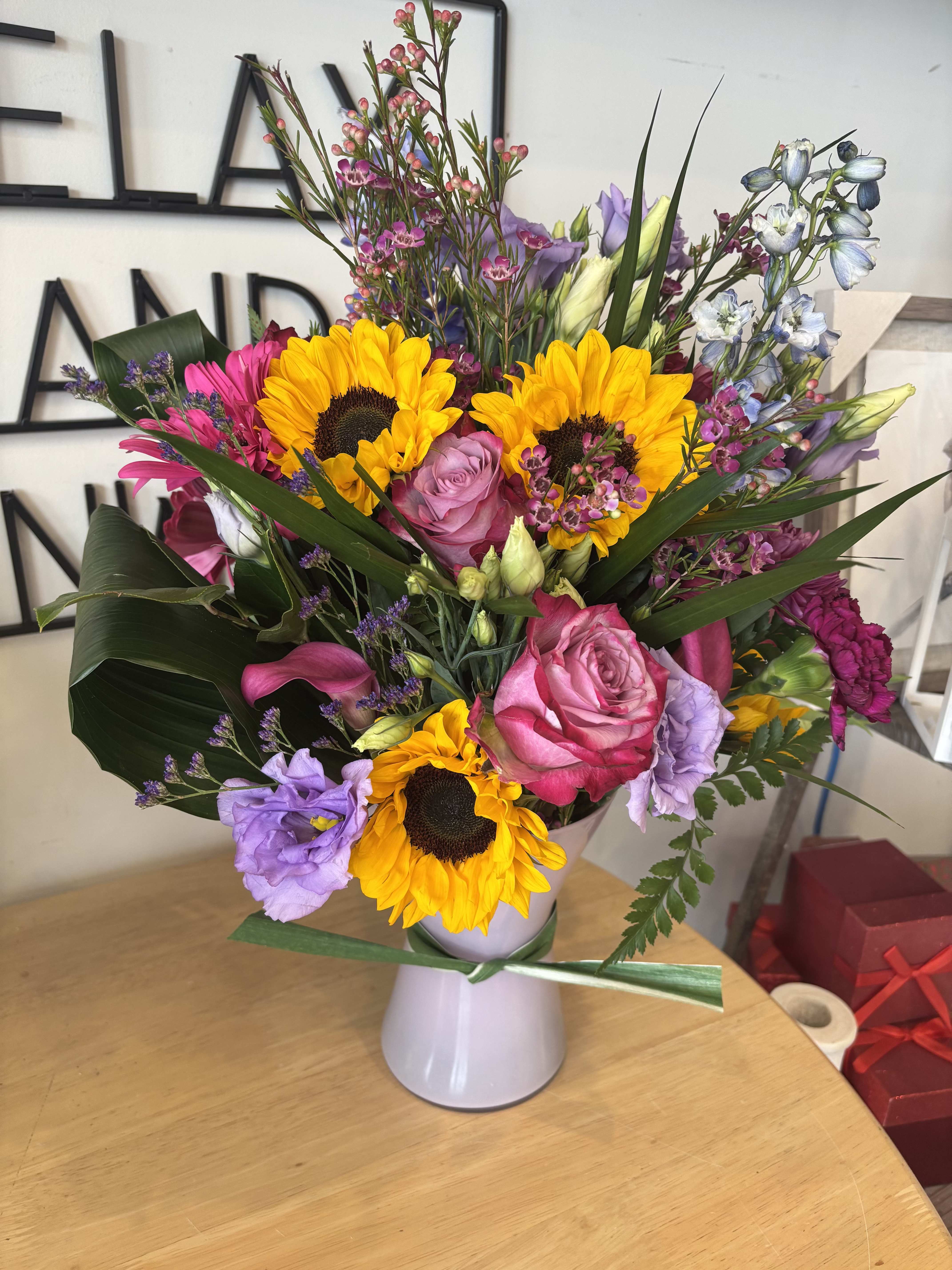 Sunny Serenity Sunny Serenity - This vibrant flower arrangement features cheerful sunflowers paired with elegant with elegant pink and purple blooms. The sunflowers bring warmth and joy, while the pink and purple flowers add a touch of charm. Perfect for any occasion, this arrangement is sure to brighten any space and convey heartfelt sentiments