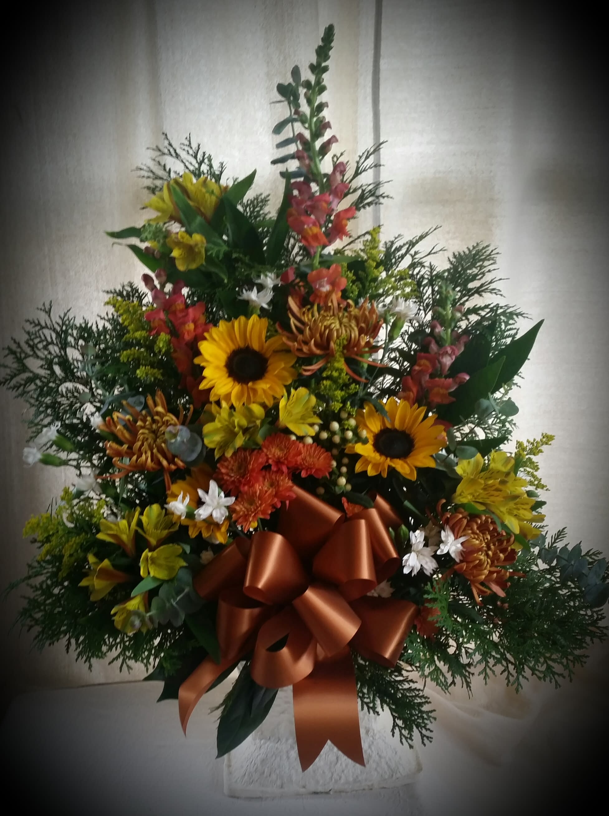 Classic funeral arrangement - This classic funeral basket is arranged in a wicker basket and has a mixture of flowers in seasonal colors--includes snapdragons, mums, sunflowers, alstroemeria and dianthus along with coordinating fillers.  You can choose to add a ribbon with script that identifies the deceased's relationship to you.