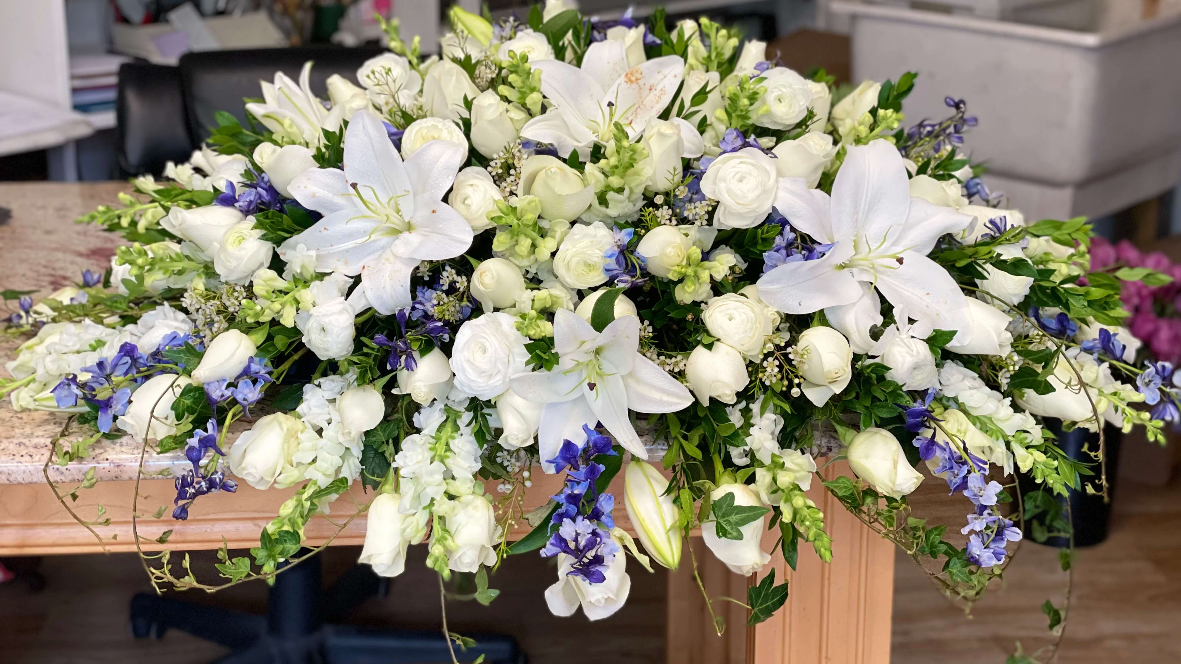 Blue and White Casket Spray Blue and White Casket Spray - Foliage includes: Lily, Rose, Ranunculus, Snapdragon, Delphinium, Wax Flower, Myrtle, and Ivy. We advise our customers to order 24-48 hours in advance of their scheduled delivery to ensure that we are able to have similar flowers and colors in the shop for their order. $600 (deluxe) as shown
