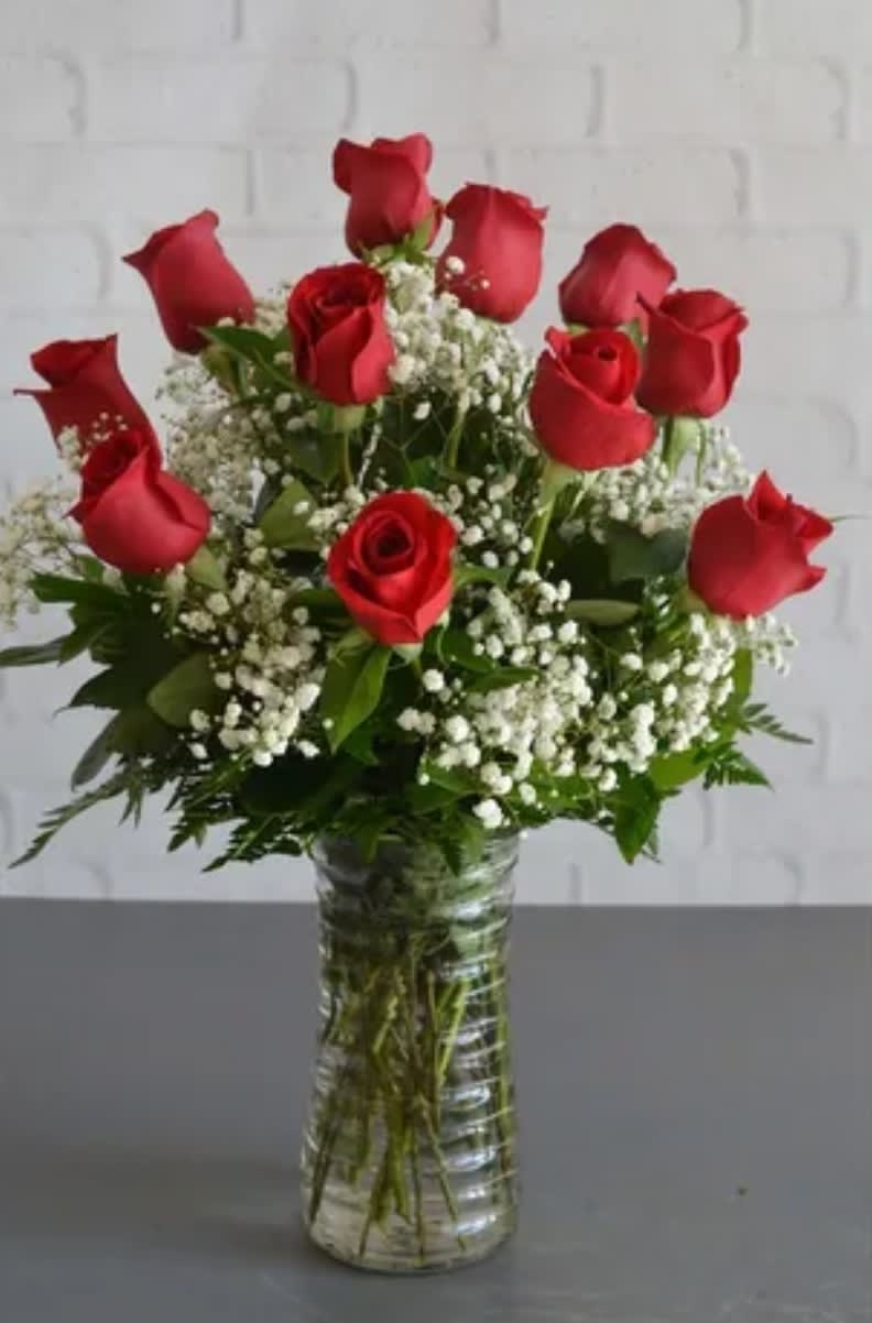 Home Run - One Dozen Red Roses arranged in a clear glass vase with greenery and filler flowers.
