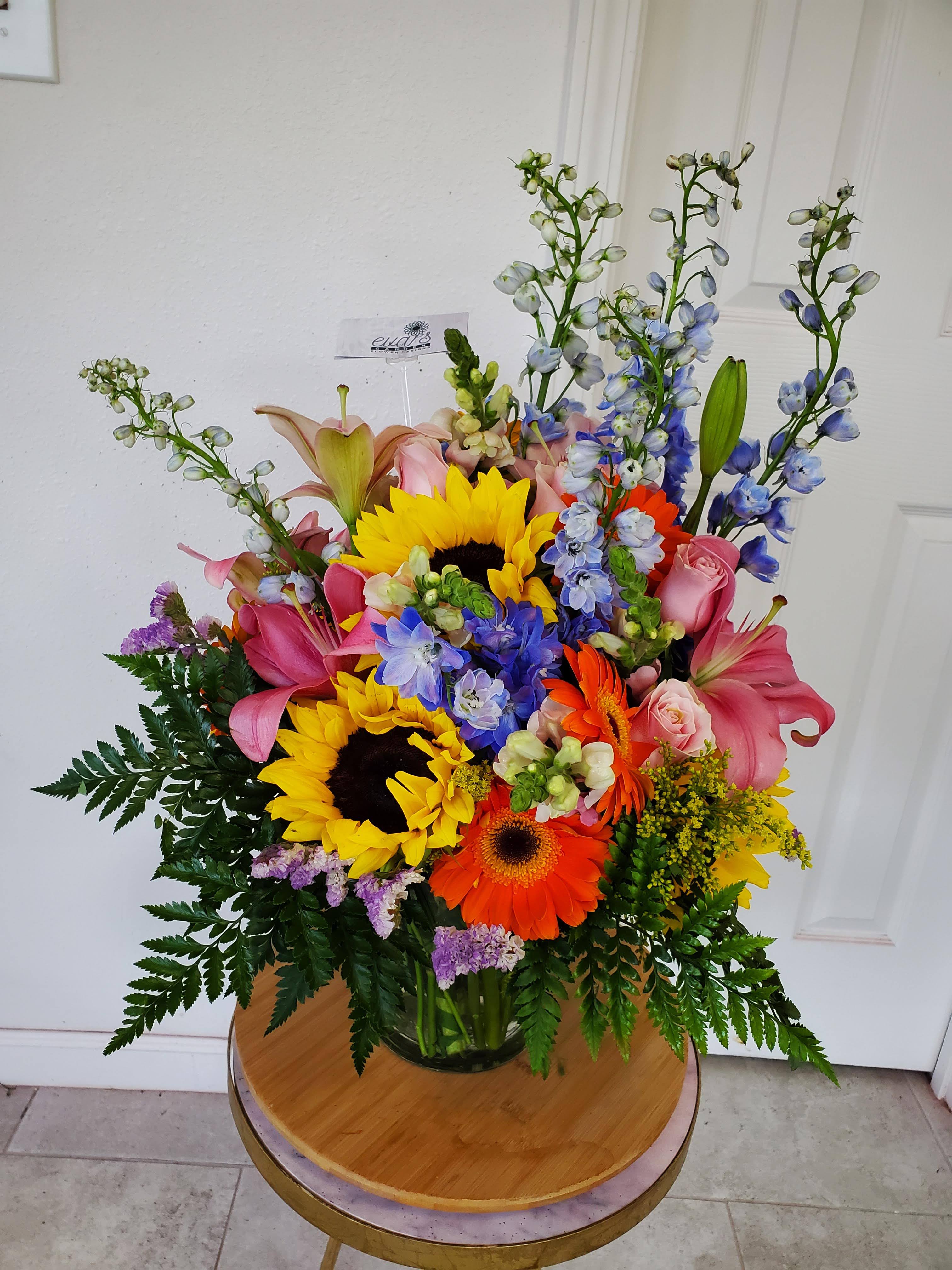 She is Sunshine Vase Arrangement She is Sunshine Vase Arrangement - Crystal vase arrangement with sunflowers, gerber daisies, delphinium, lilies, and snapdragons in spring colors. (Picture depicts a premium product; standard & deluxe size available upon request)