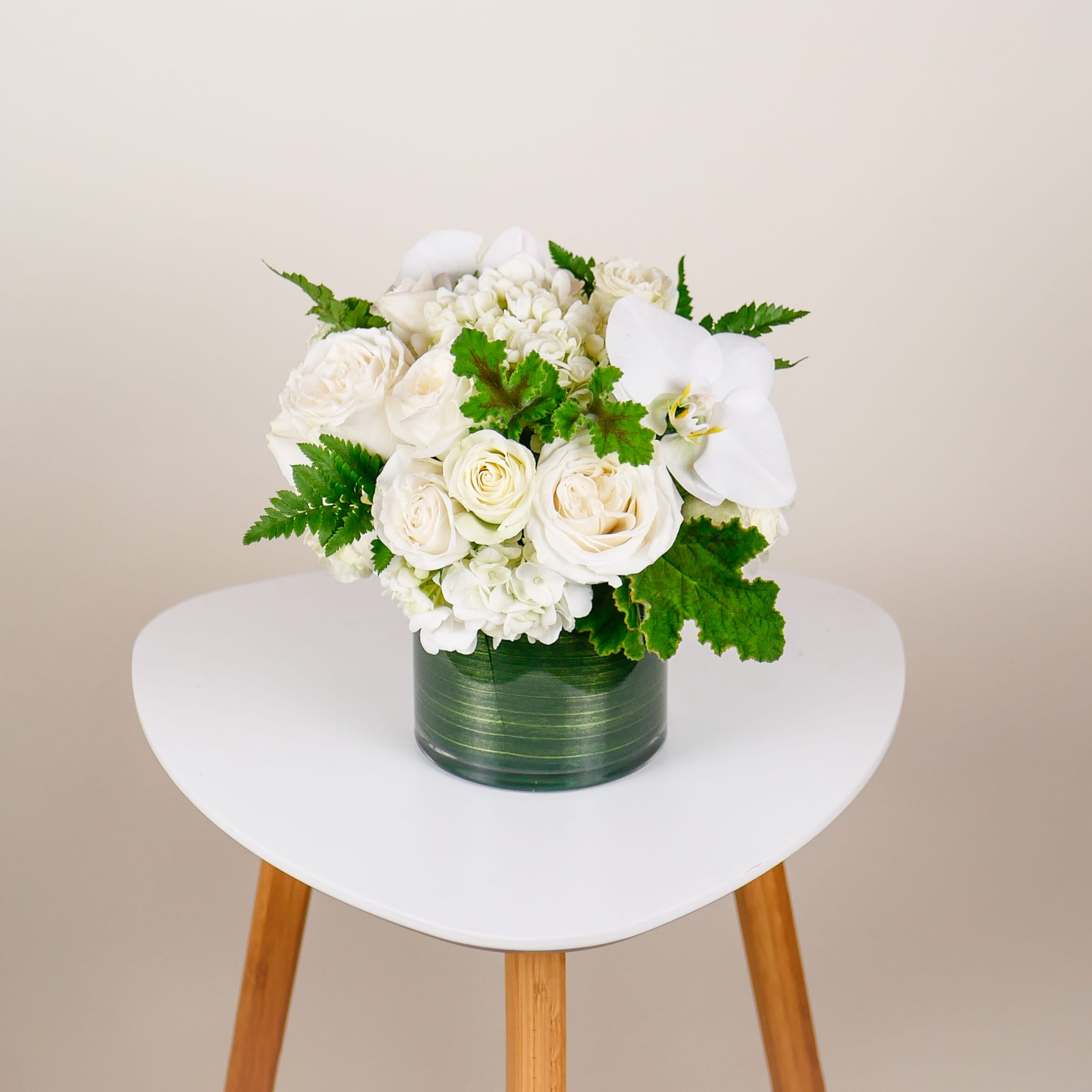 Cherished Moments - This delicate arrangement uses a lush, compact design to showcase beautiful Playa Blanca white roses, orchid accents, spray roses, and premium hydrangeas elegantly arranged in a 5&quot; leaf-lined cylinder vase.