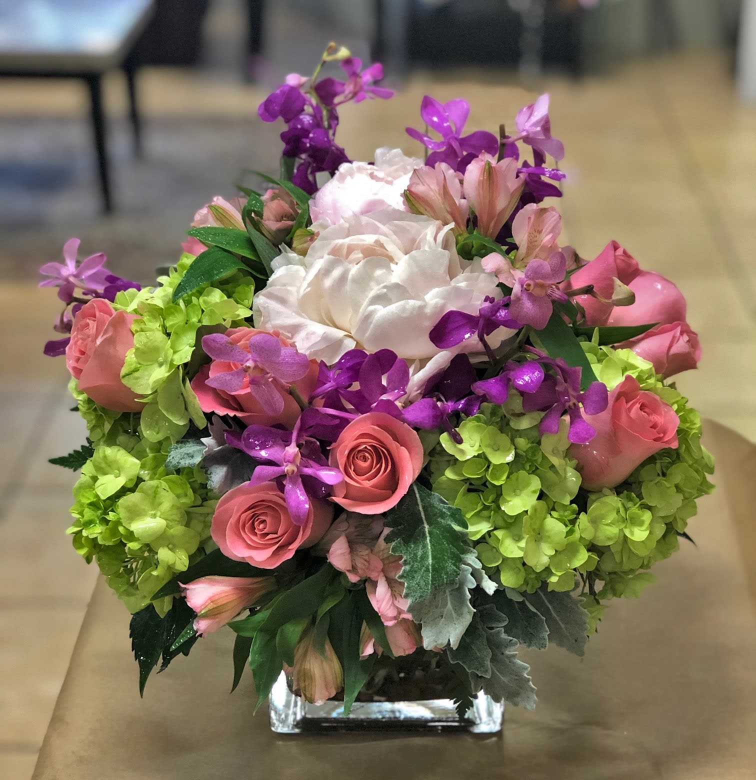 Warm thoughts - Elevate your space with our modern floral arrangement, a true testament to contemporary elegance. Featuring delicate blush pink roses, vibrant green hydrangeas, exotic orchids, and more, this arrangement is a captivating blend of sophistication and style. Each stem is expertly curated and skillfully arranged in a leaf-lined glass cylinder vase, adding a sleek and streamlined touch to the overall design. Perfect for adding a touch of modern flair to any room, this arrangement is ideal for special occasions, corporate settings, or as a statement piece in your home. Embrace the beauty of modern aesthetics with this exquisite floral masterpiece. 