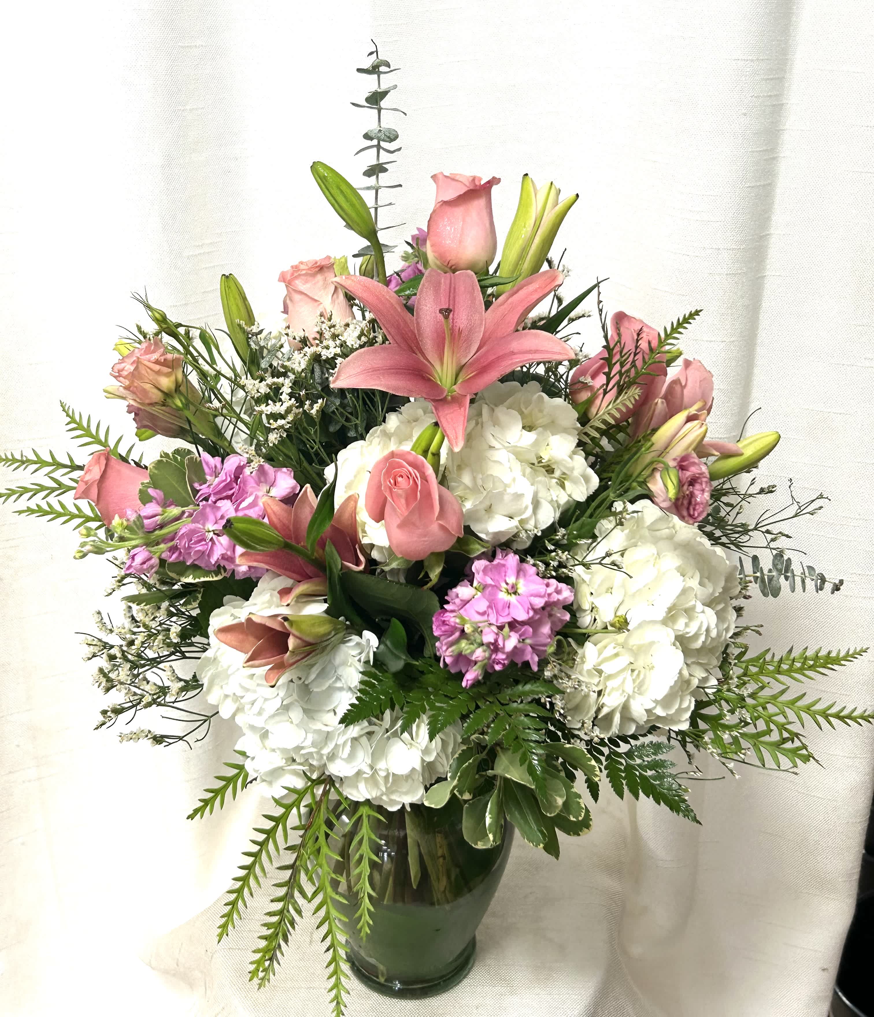 Gentle Melodies - Celebrate the beauty of nature with our exquisite flower arrangement, a harmonious blend of elegance and charm. This stunning composition features delicate roses and fragrant hydrangeas, complemented by the lush blooms of stock, lilies, and lisianthus. The vibrant hues and graceful shapes of these flowers intertwine to create a mesmerizing display of natural splendor. Accented with verdant greens and filler, this arrangement exudes a sense of tranquility and opulence, making it a perfect choice for any special occasion or as a thoughtful gesture to brighten someone's day. Whether as a centerpiece at a gathering or a thoughtful gift, this arrangement is sure to leave a lasting impression of beauty and grace.