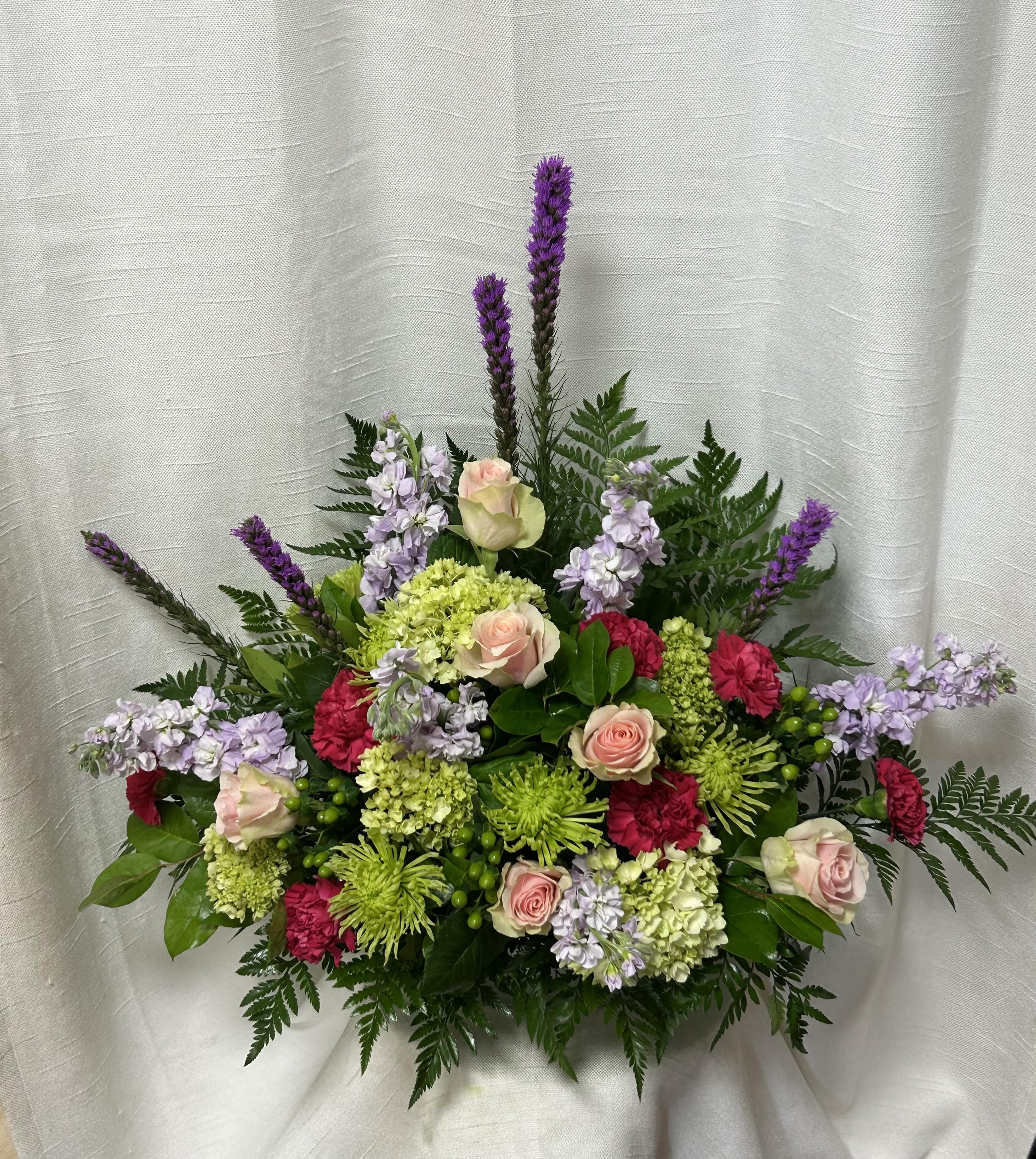 Warm Caress - Create a heartfelt tribute with our funeral flower arrangement, featuring a delicate combination of green Fuji mums, purple stock, hot pink roses, hot pink carnations, hot pink mini carnations, green hypericum berries, and lush greenery. This stunning arrangement conveys a message of love, remembrance, and sympathy, honoring the life and memory of your loved one.