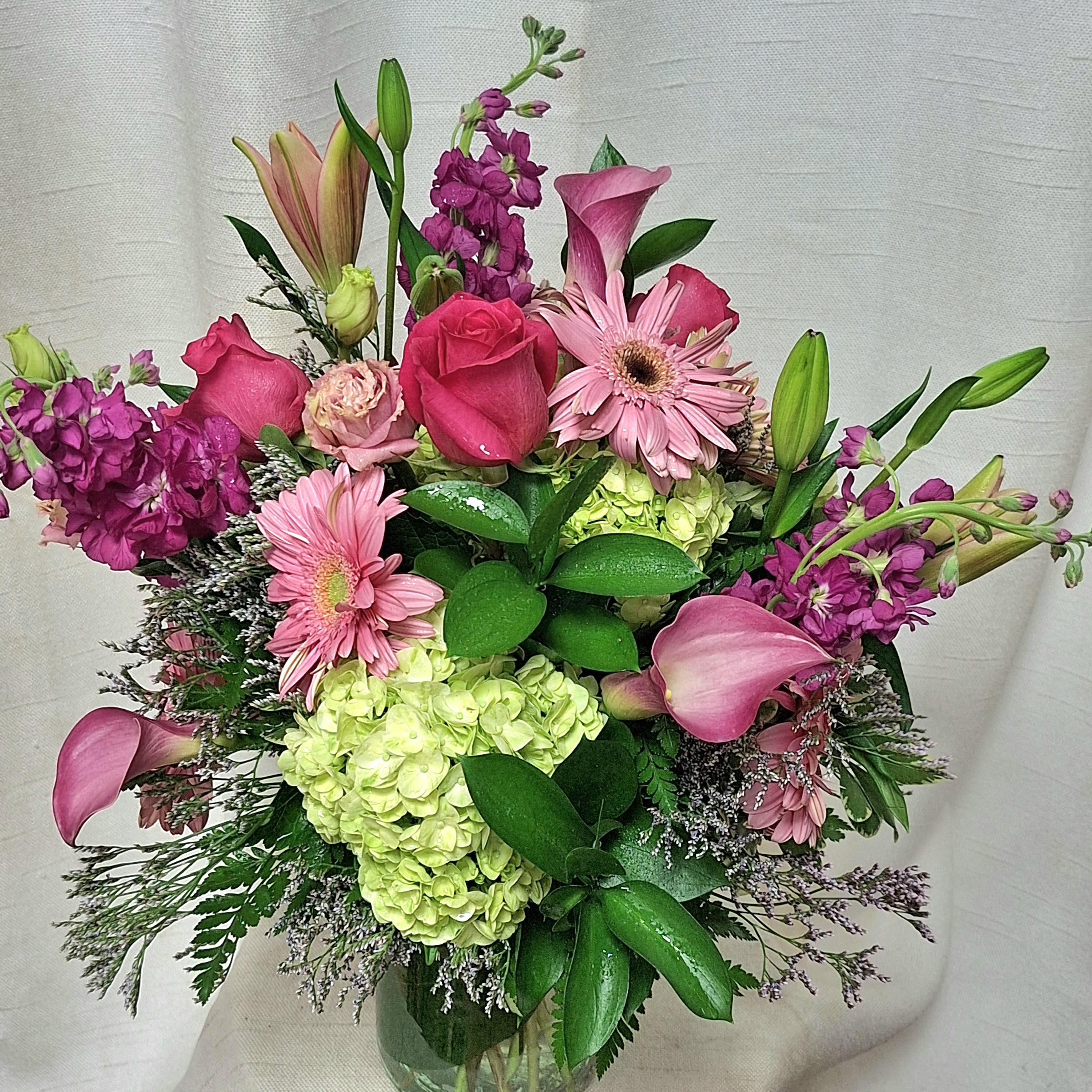 Whimsical - This captivating flower arrangement combines the classic beauty of roses, the fragrant allure of stock, the elegant charm of lilies, and the lush fullness of hydrangea. Soft, delicate roses provide a romantic focal point, while the sweet aroma of stock fills the air. 