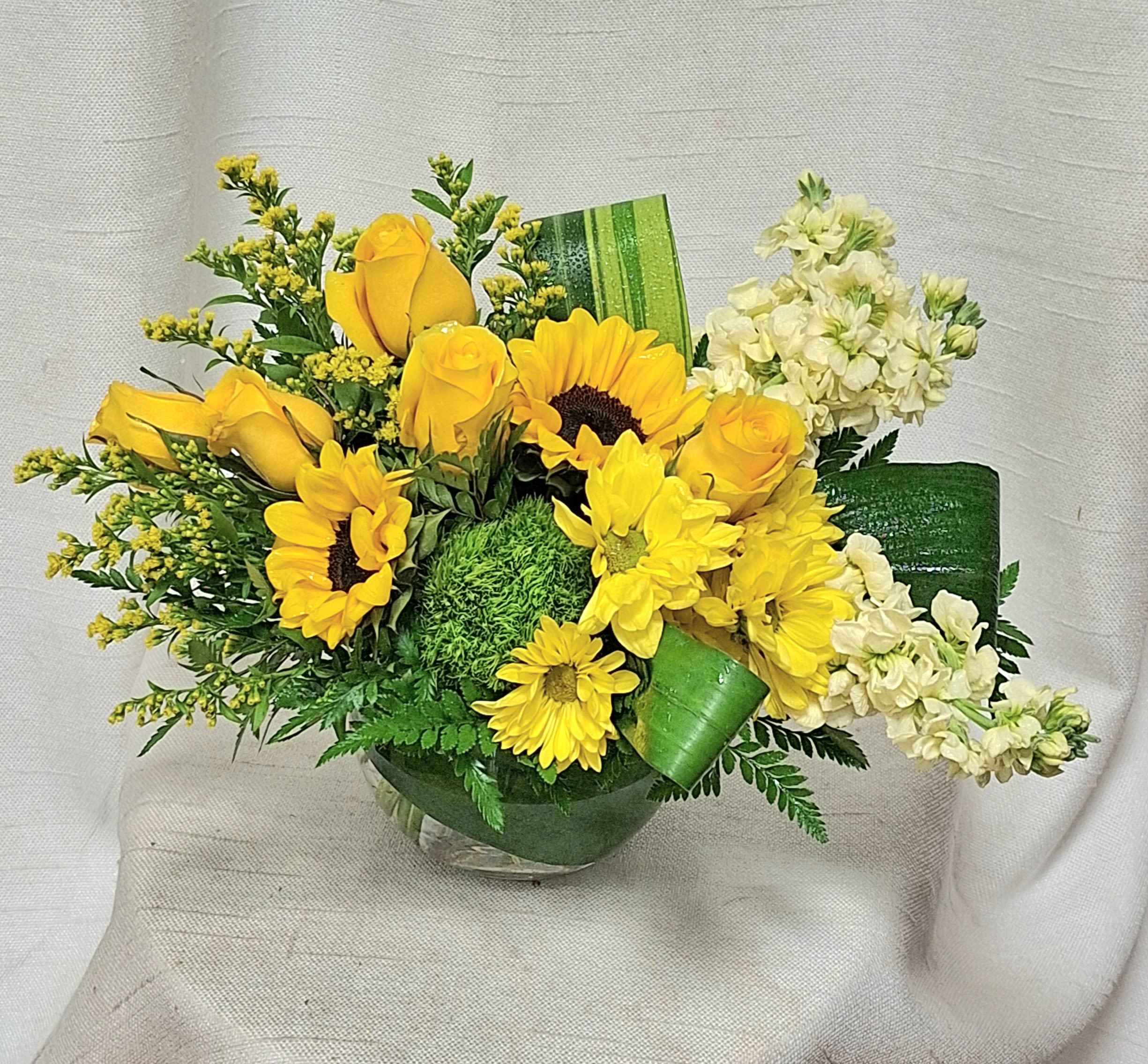 Spectacular Sunlight - This vibrant flower arrangement is a celebration of sunshine, joy, and positivity, featuring a harmonious blend of blooms in shades of yellow and green. From the whimsical green trick dianthus to the classic beauty of yellow roses and the cheerful presence of sunflowers, each stem in this composition adds a touch of warmth and luminosity, creating a symphony of colors and textures that will brighten any space and uplift the spirit.