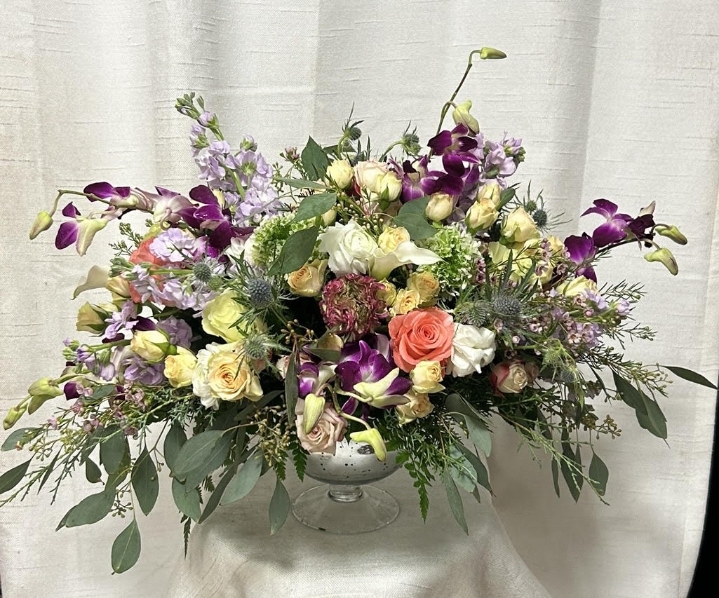 Positively Perfect - Introducing our stunning modern floral arrangement, an exquisite combination of pink, peach, and lavender roses, spray roses, lisianthus, and more. This contemporary masterpiece is expertly arranged in a pedestal vase, adding an extra touch of elegance and sophistication to the design.  