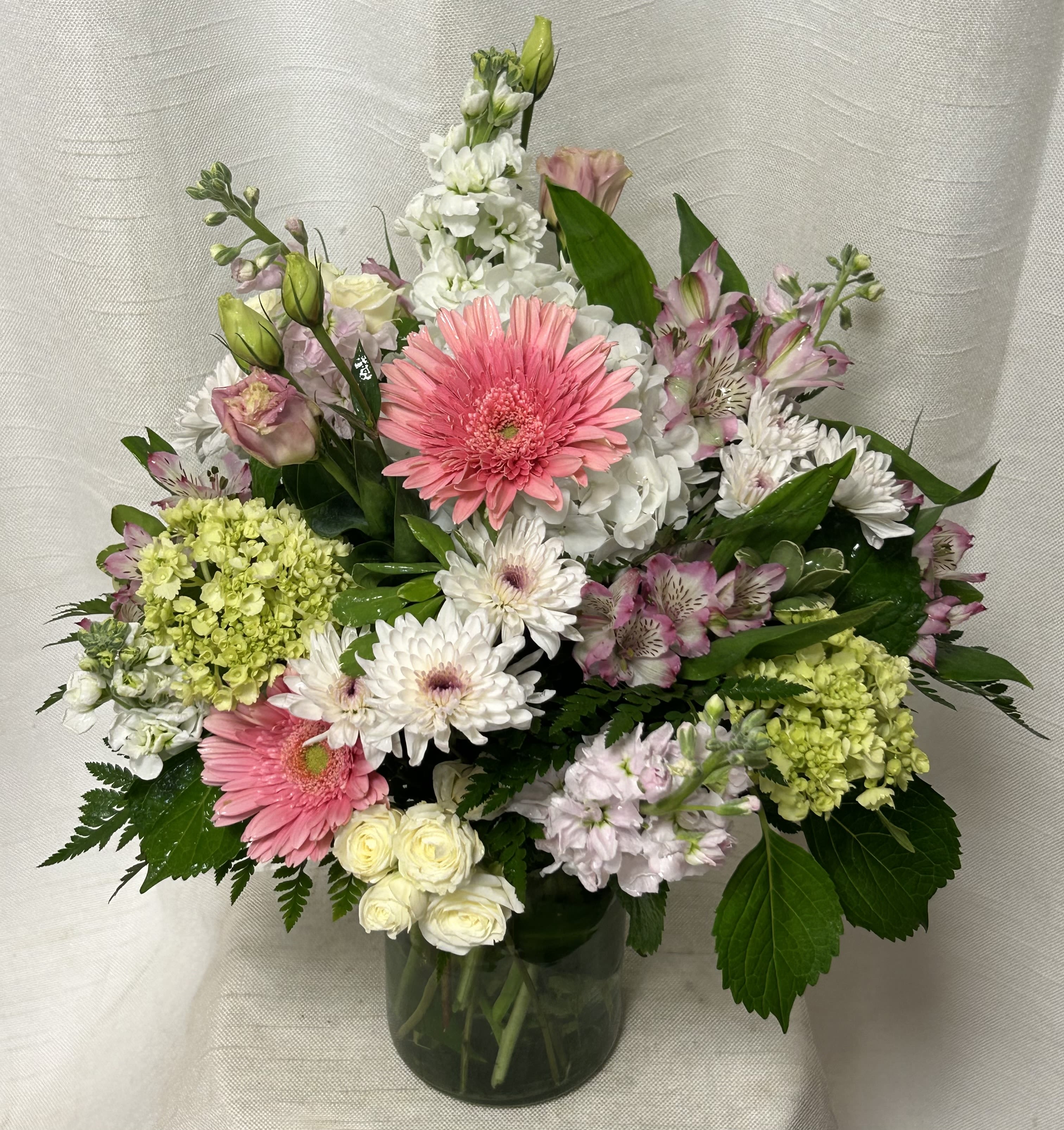 Pastel Petals - Indulge in a symphony of soft hues and charming blooms with our &quot;Pastel Petals&quot; flower arrangement. This delightful ensemble is a celebration of tender beauty, showcasing a captivating blend of pink gerbera daisies, snow-white daisies, delicate pink alstroemeria, lush green and white hydrangea, blush-pink stock, pure white spray roses, and romantic pink lisianthus.