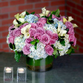 Precious One  - Indulge in the exquisite luxury of our upscale flower arrangement, expertly designed to showcase the captivating beauty of purple roses, blue hydrangeas, and white mini calla lilies. This stunning composition is presented in a large glass cylinder vase, creating a sense of grandeur and elegance.  