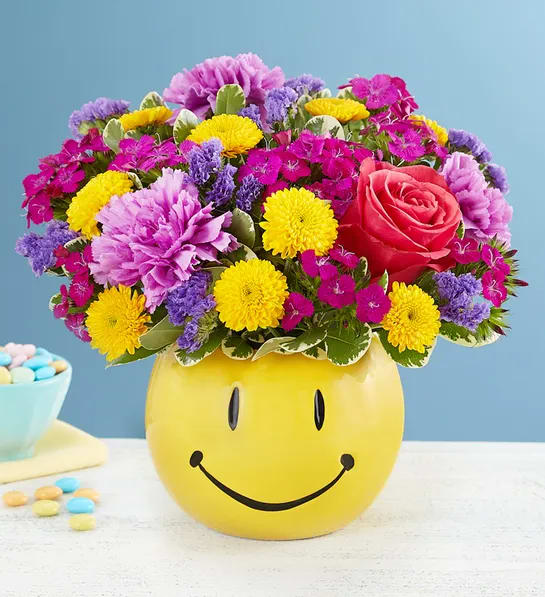 Good Day™ Bouquet Good Day™ Bouquet - EXCLUSIVE Helping you deliver smiles is what we do…and this feel-good bouquet is a great way to do it! Bunches of blooms in uplifting colors are gathered into our keepsake smiley face container, delivering just the brightness they need to make their day better. Perfect for celebration-worthy moments and everyday sentiments. All-around arrangement with hot pink roses, yellow button poms, lavender carnations, purple dianthus and statice; accented with assorted greenery Artistically designed in our ceramic smiley face container; measures 4.5"H x 5.5"W Arrangement measures approximately 10"H x 9"W Our florists hand-design each arrangement, so colors and varieties may vary due to local availability